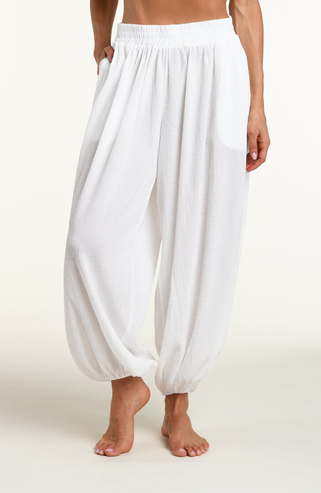 Woman wearing white crochet style beach pants against a white background. 