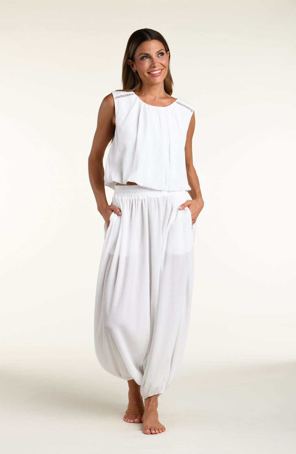 Woman wearing white crochet style beach pants and matching sleeveless top against a white background. 