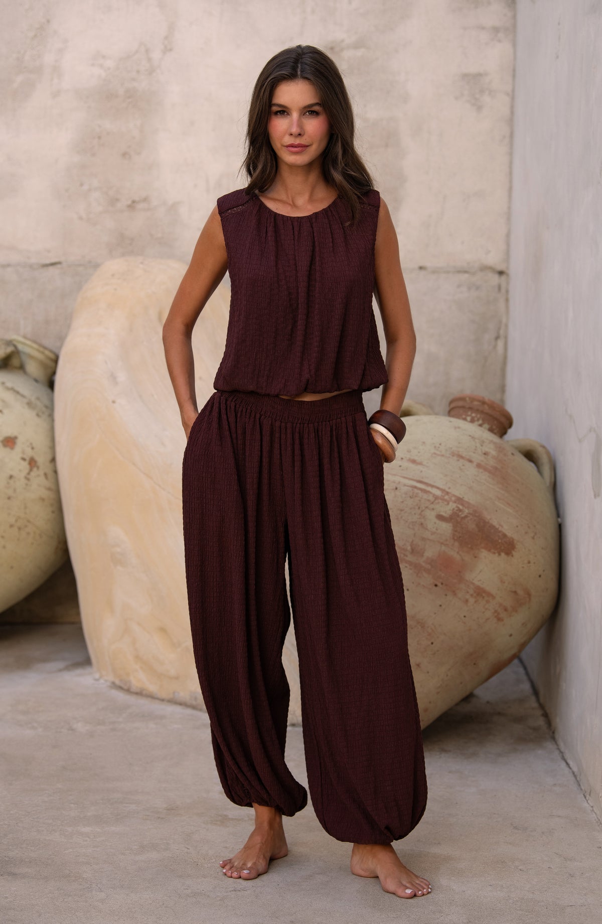 Woman wearing a java brown colored sleeveless top and matching pants against a light brown background. 