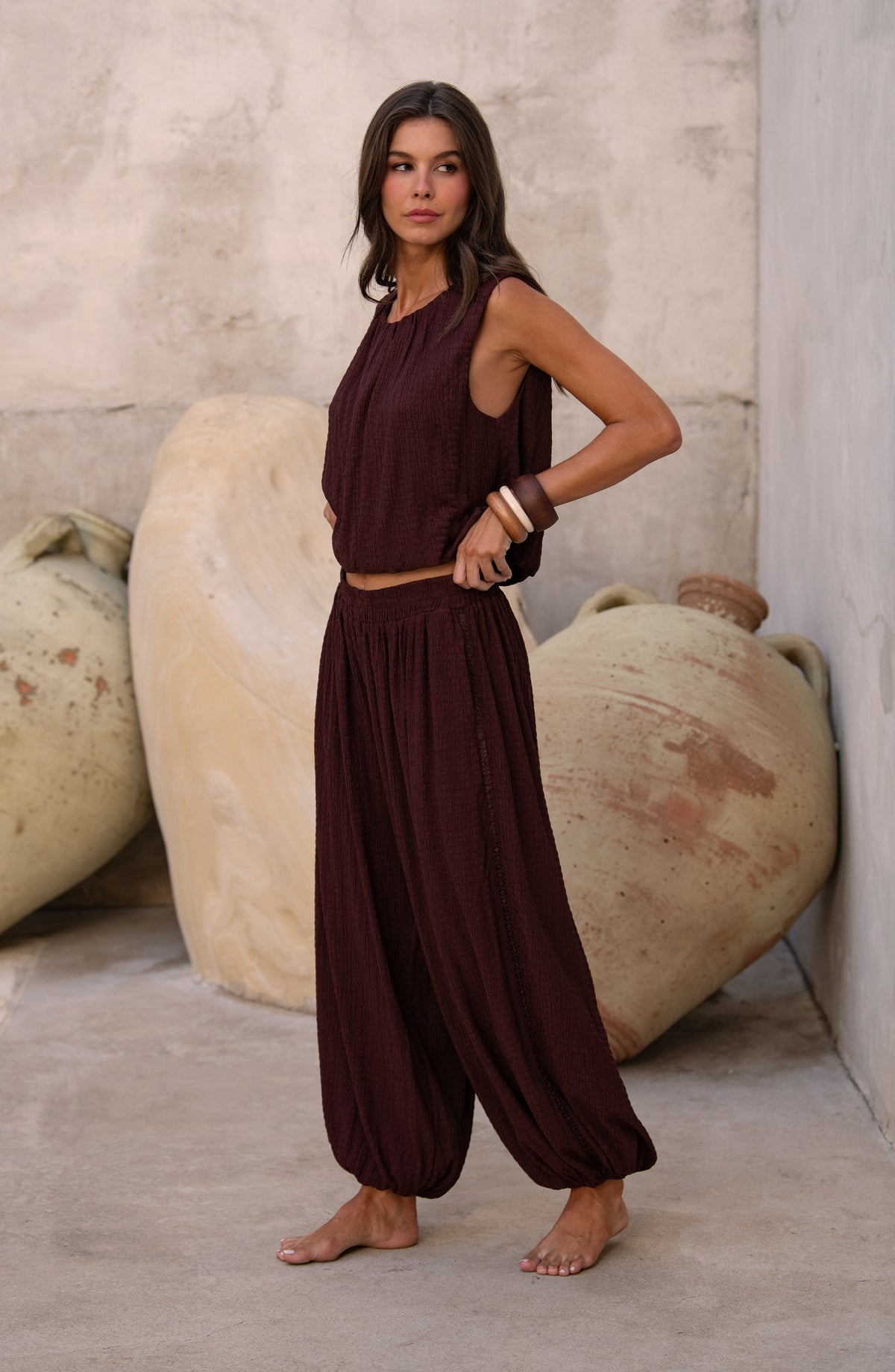 Woman wearing a java brown colored sleeveless top and matching pants against a light brown background. 