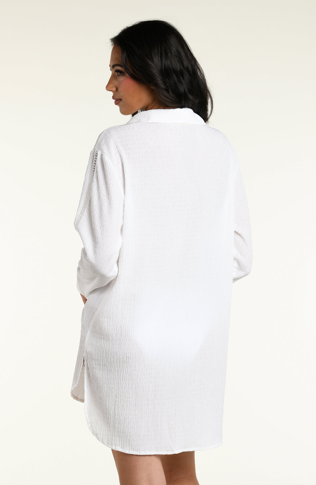 Woman wearing a white long sleeve cover up top against a white background. 