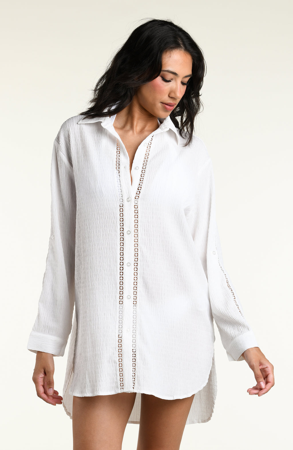 Woman wearing a white long sleeve cover up top against a white background. 