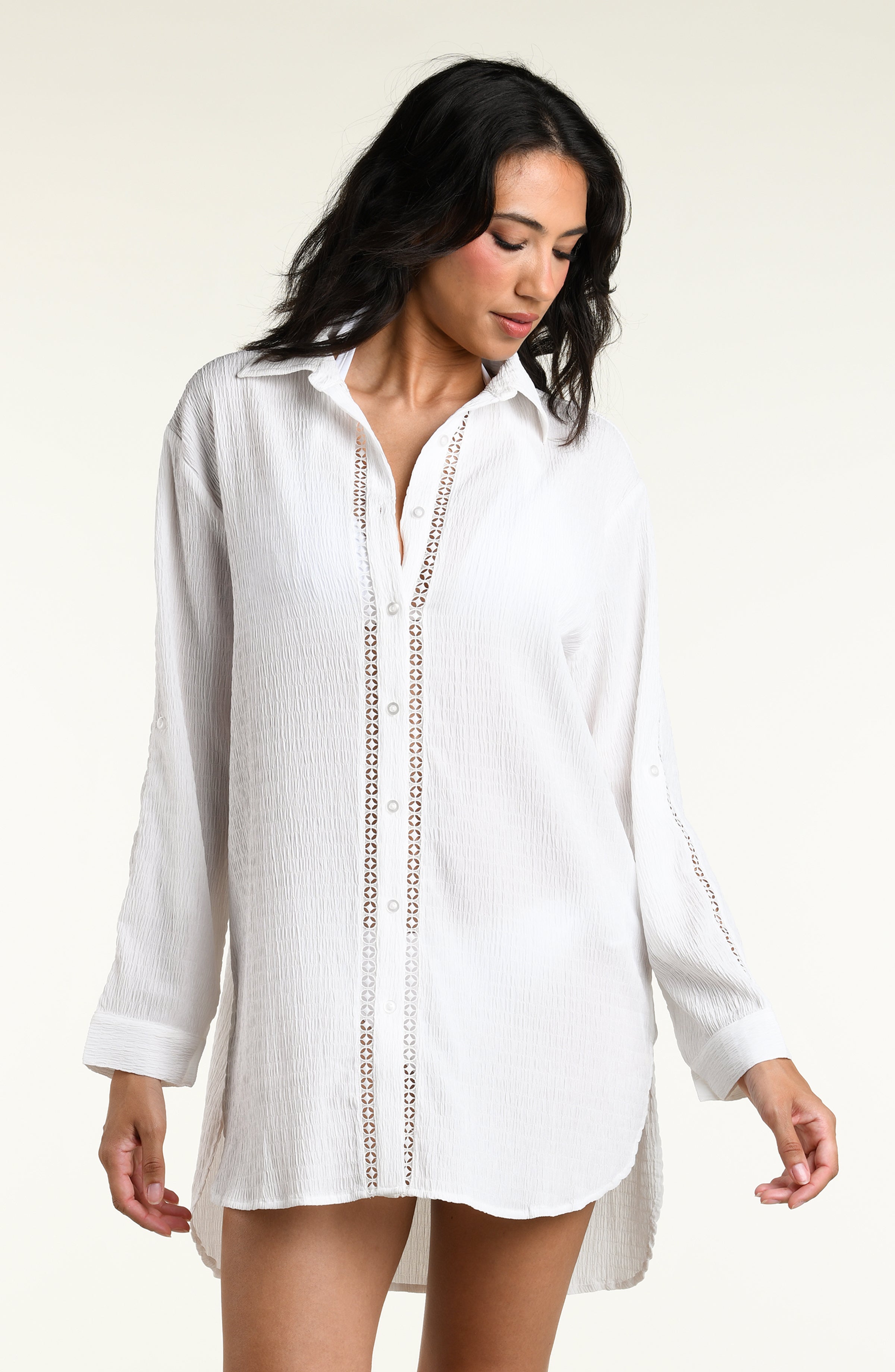 Woman wearing a white long sleeve cover up top against a white background. 