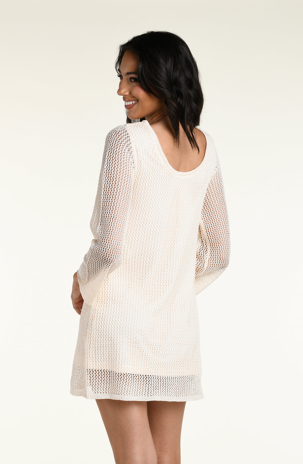 A woman modeling a cream-colored, open-knit three-quarter sleeve mini dress against a white background. 