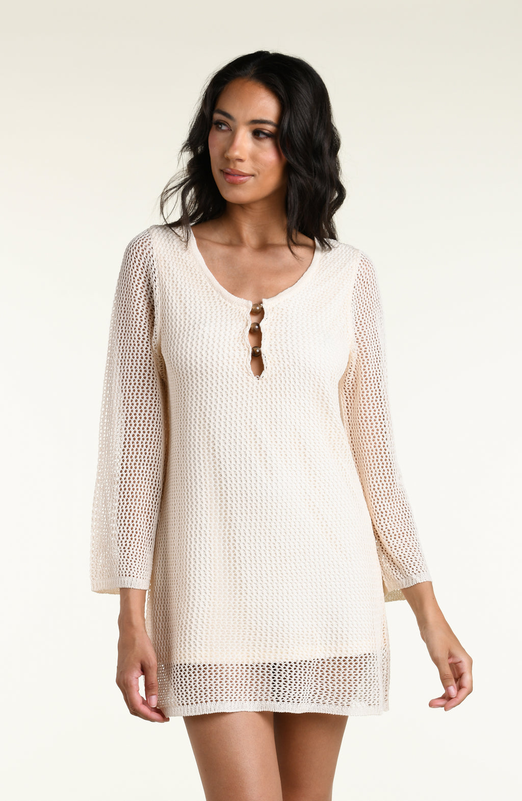 A woman modeling a cream-colored, open-knit three-quarter sleeve mini dress against a white background. 