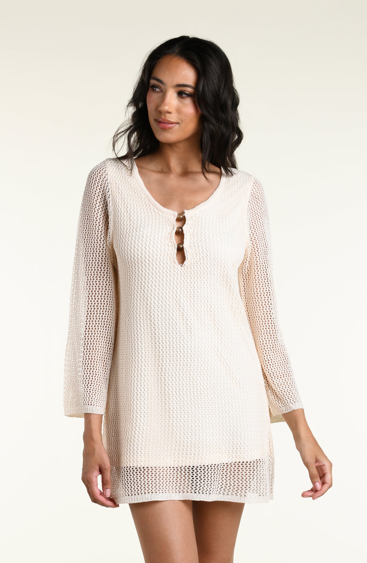 A woman modeling a cream-colored, open-knit three-quarter sleeve mini dress against a white background. 