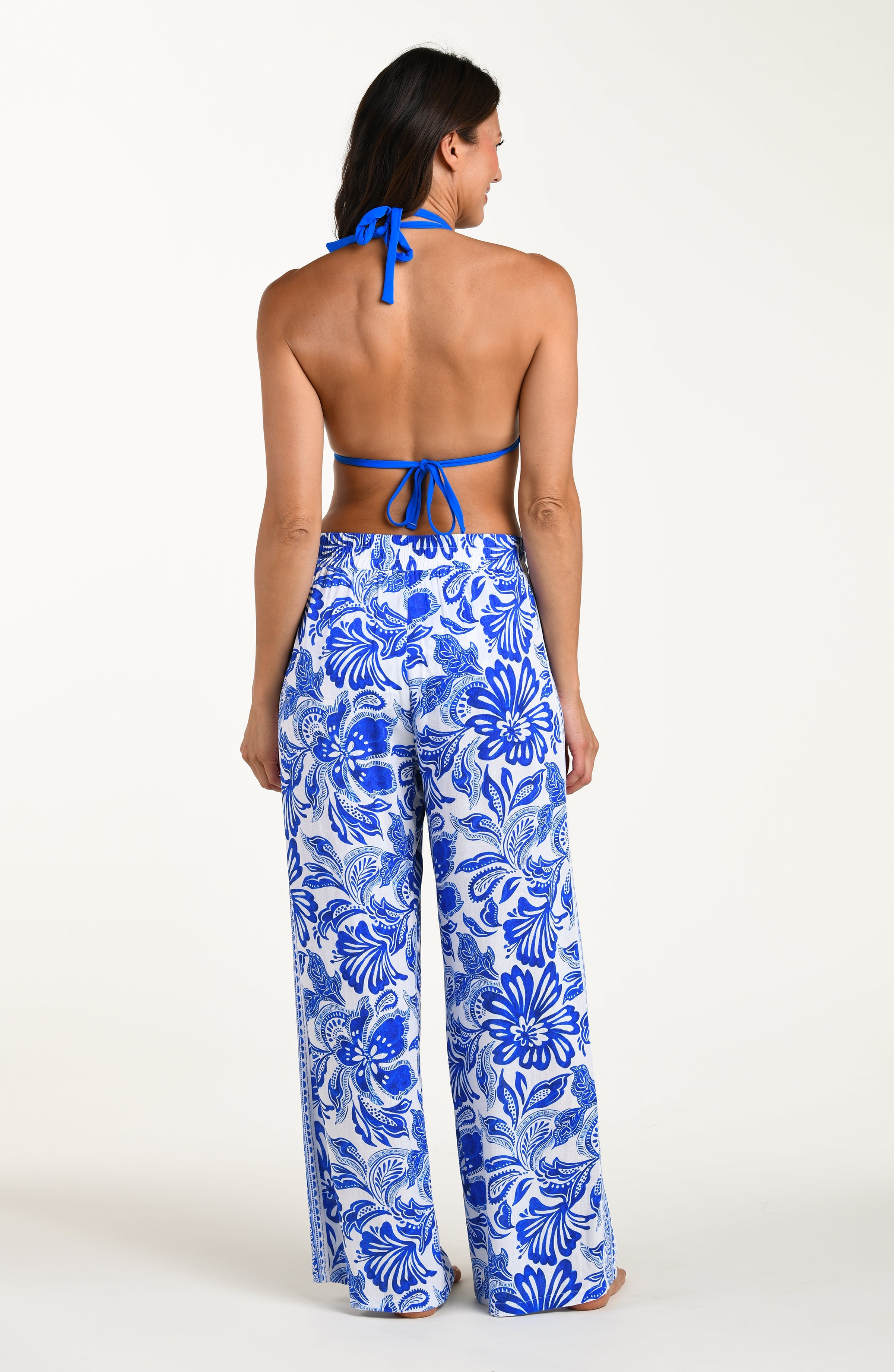 Woman wearing a blue bikini top and floral pants on a white background