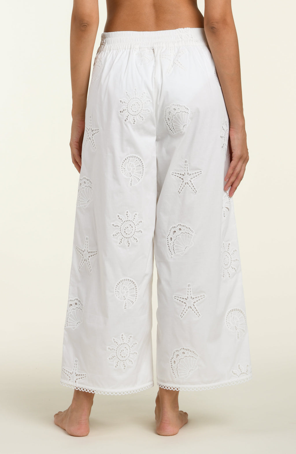 Woman wearing white cover up pants against a white background. 