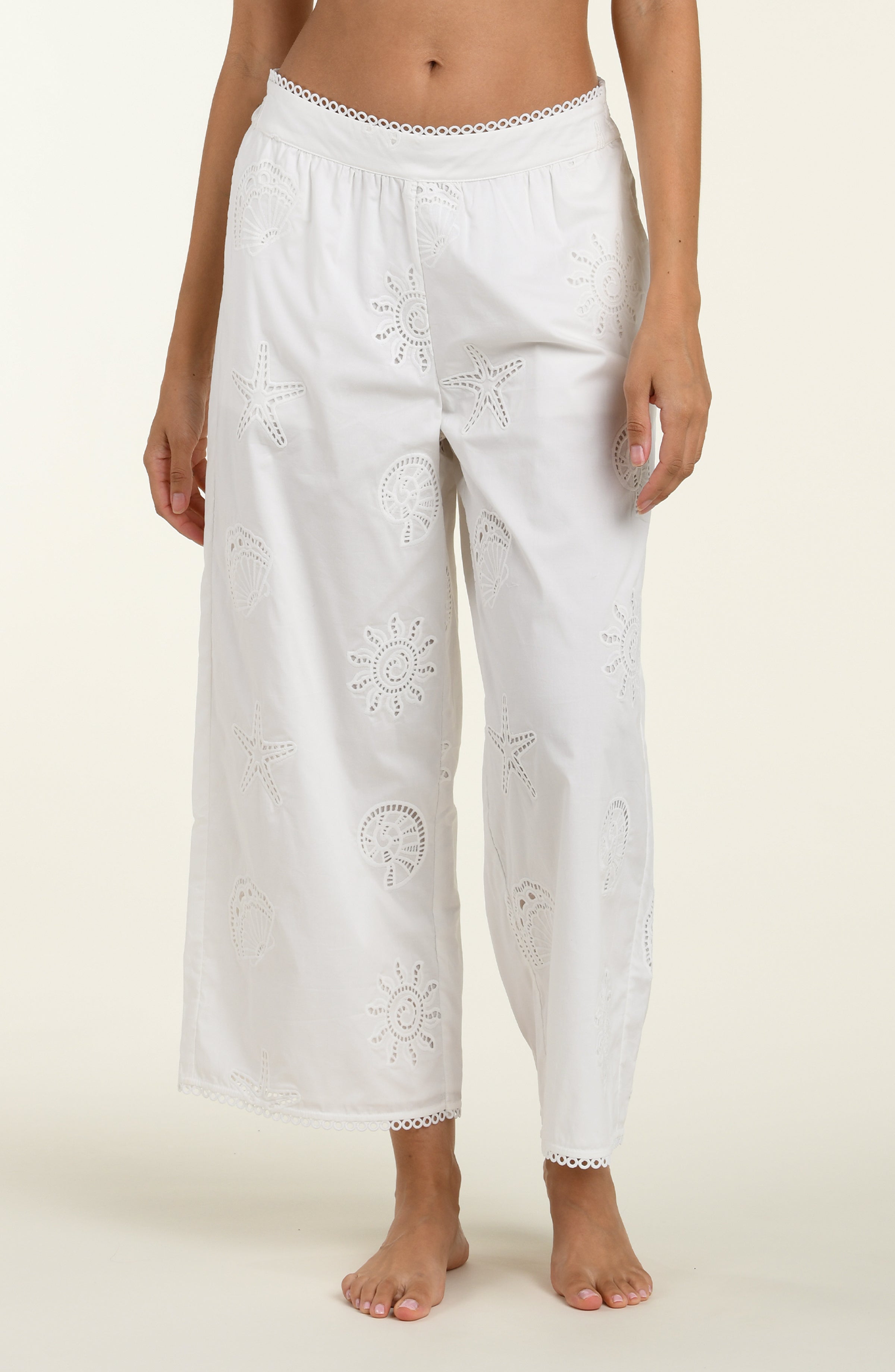 Woman wearing white cover up pants against a white background. 