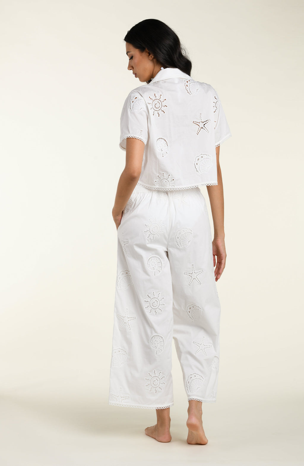 Woman wearing a white cover up shirt with matching pants against a white background. 