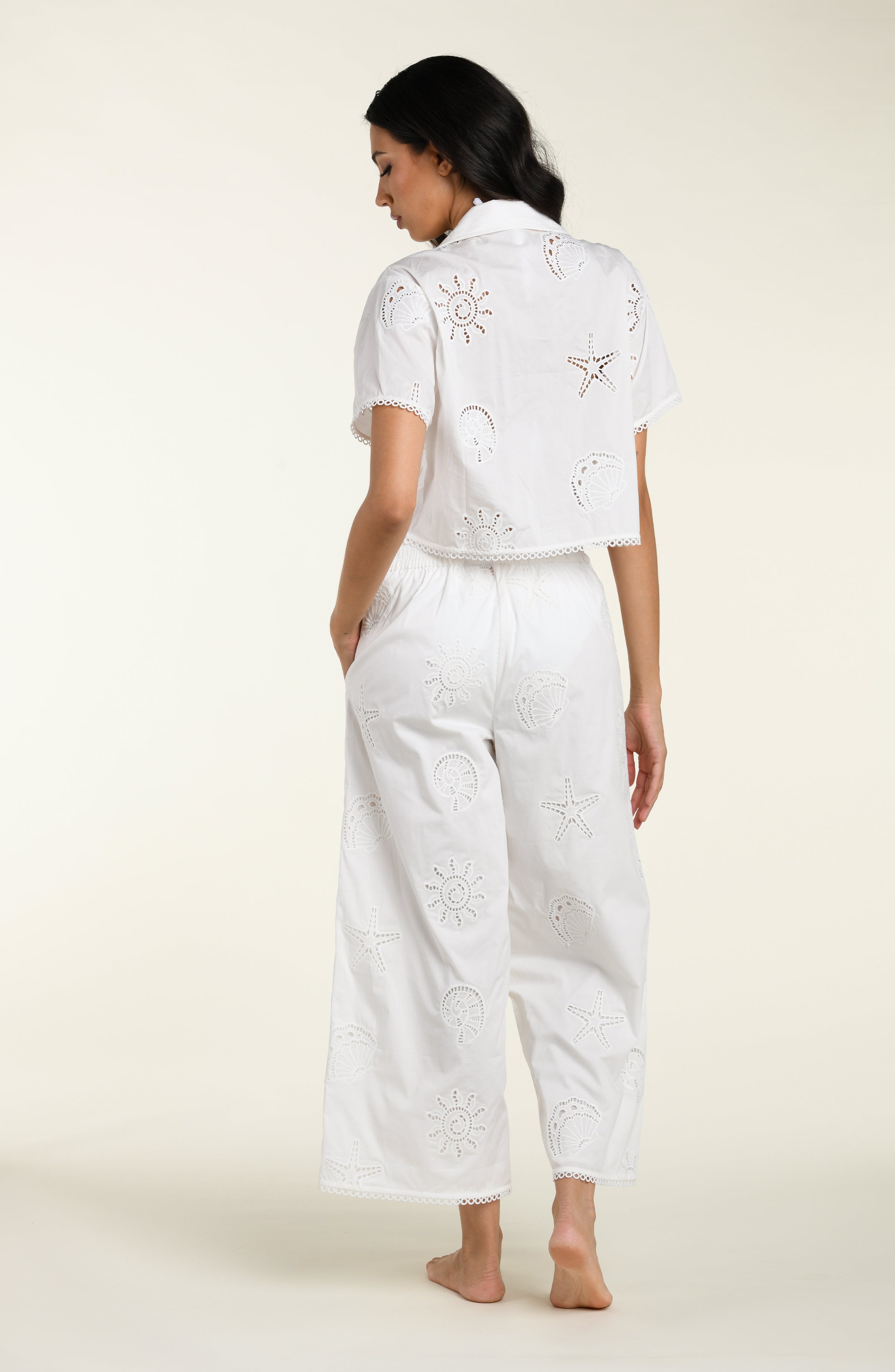 Woman wearing a white cover up shirt with matching pants against a white background. 