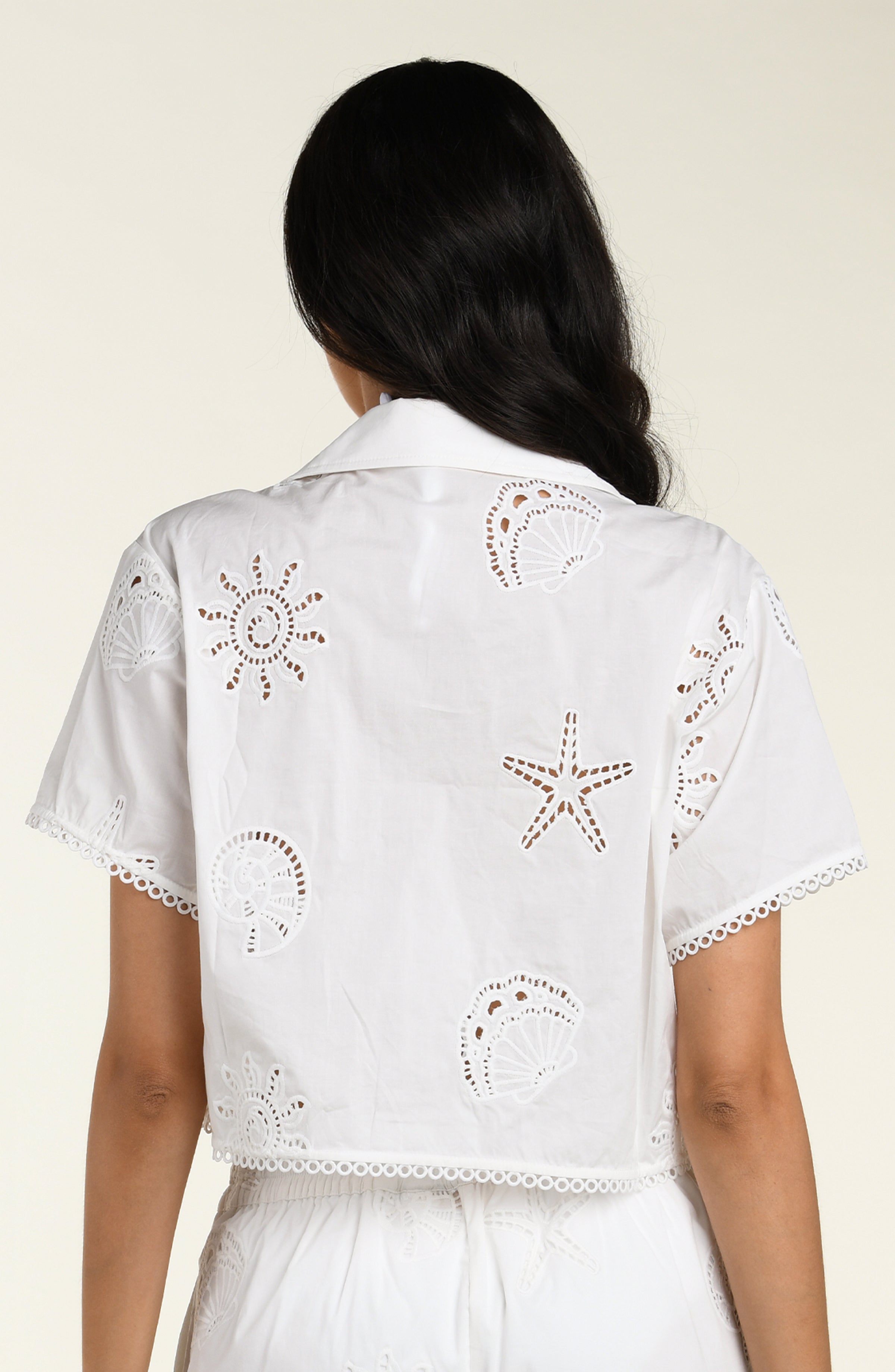 Woman wearing a white cover up shirt with matching pants against a white background. 