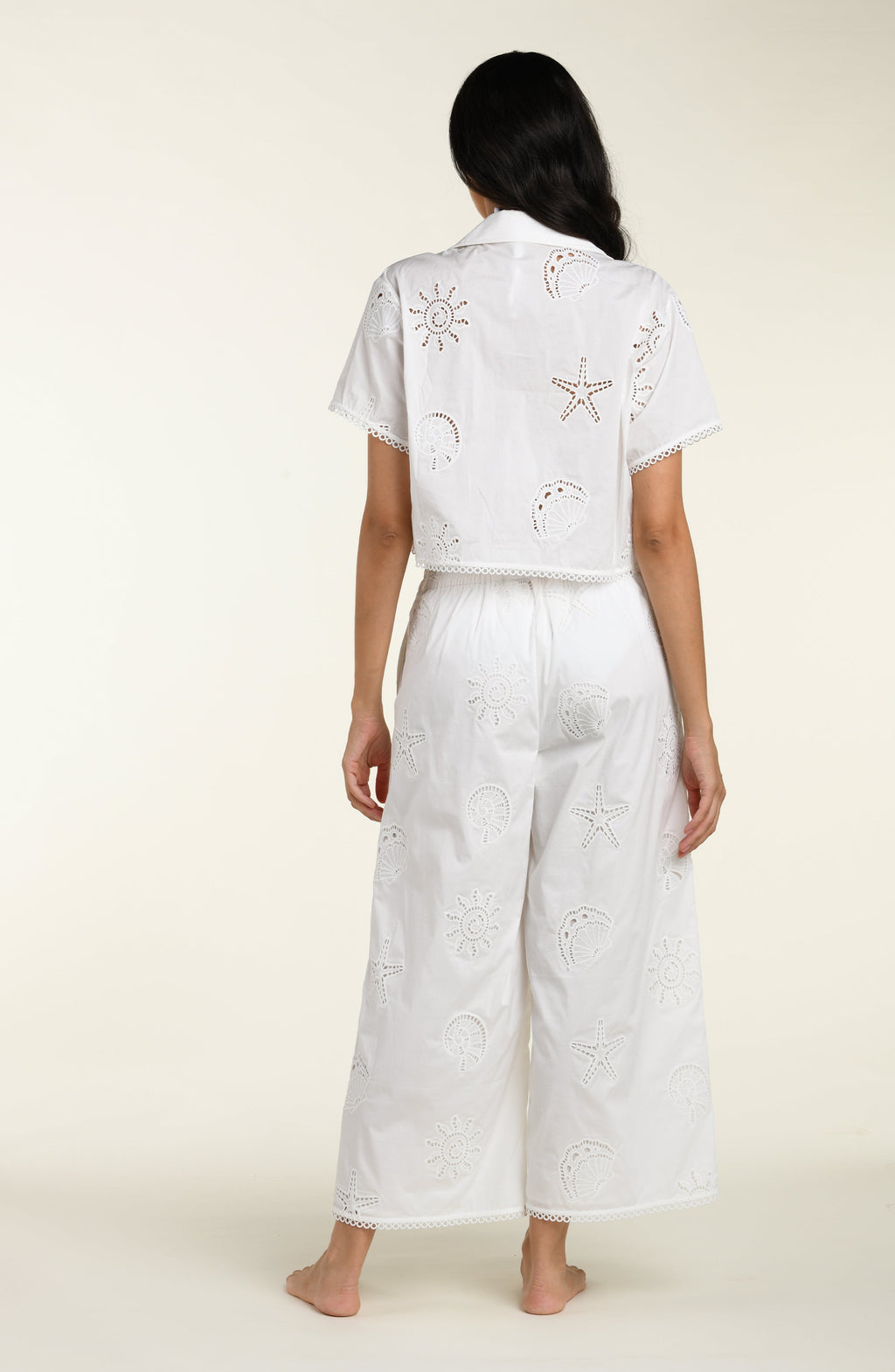 Woman wearing a white cover up shirt with matching pants against a white background. 
