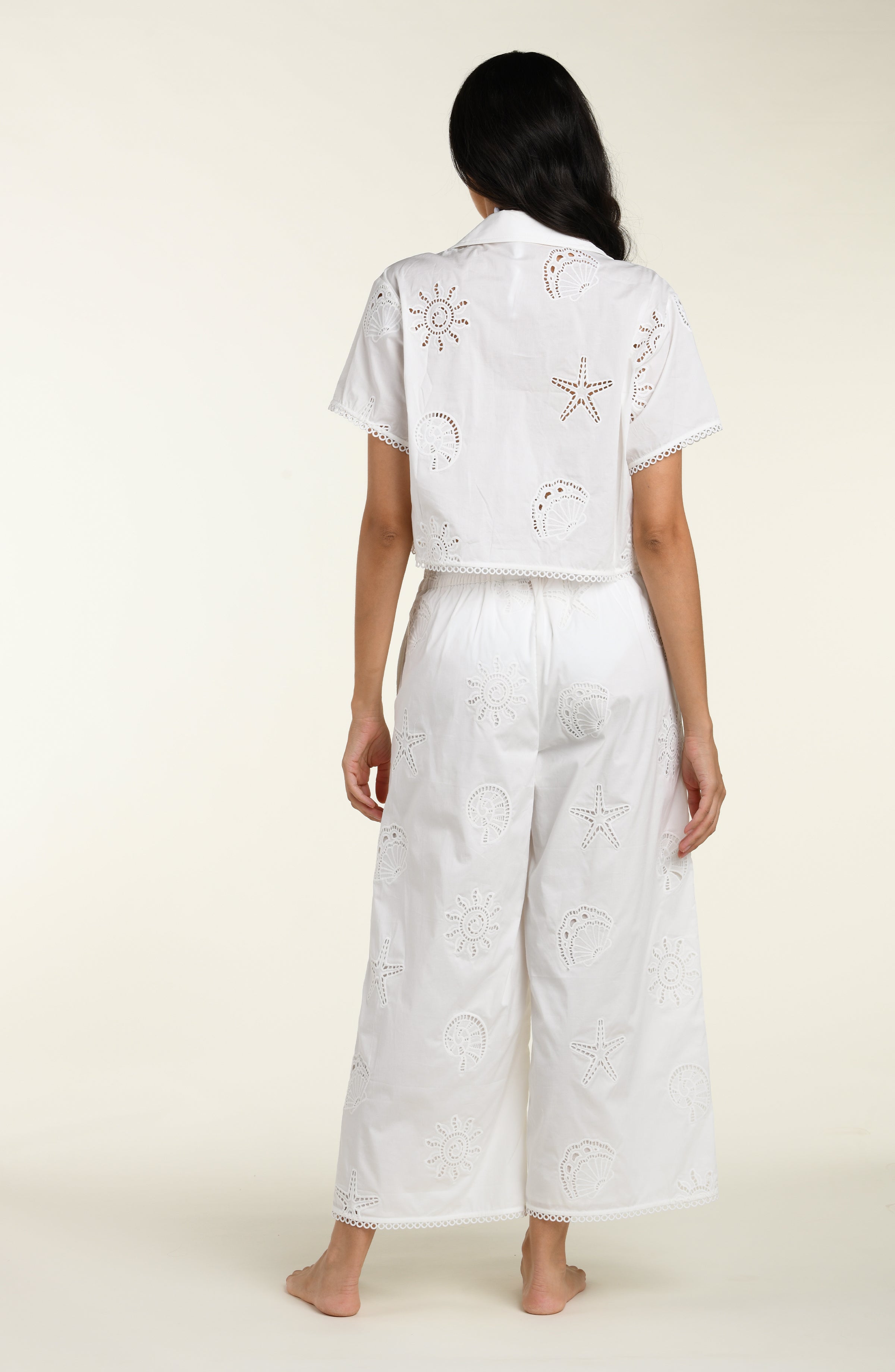 Woman wearing a white cover up shirt with matching pants against a white background. 