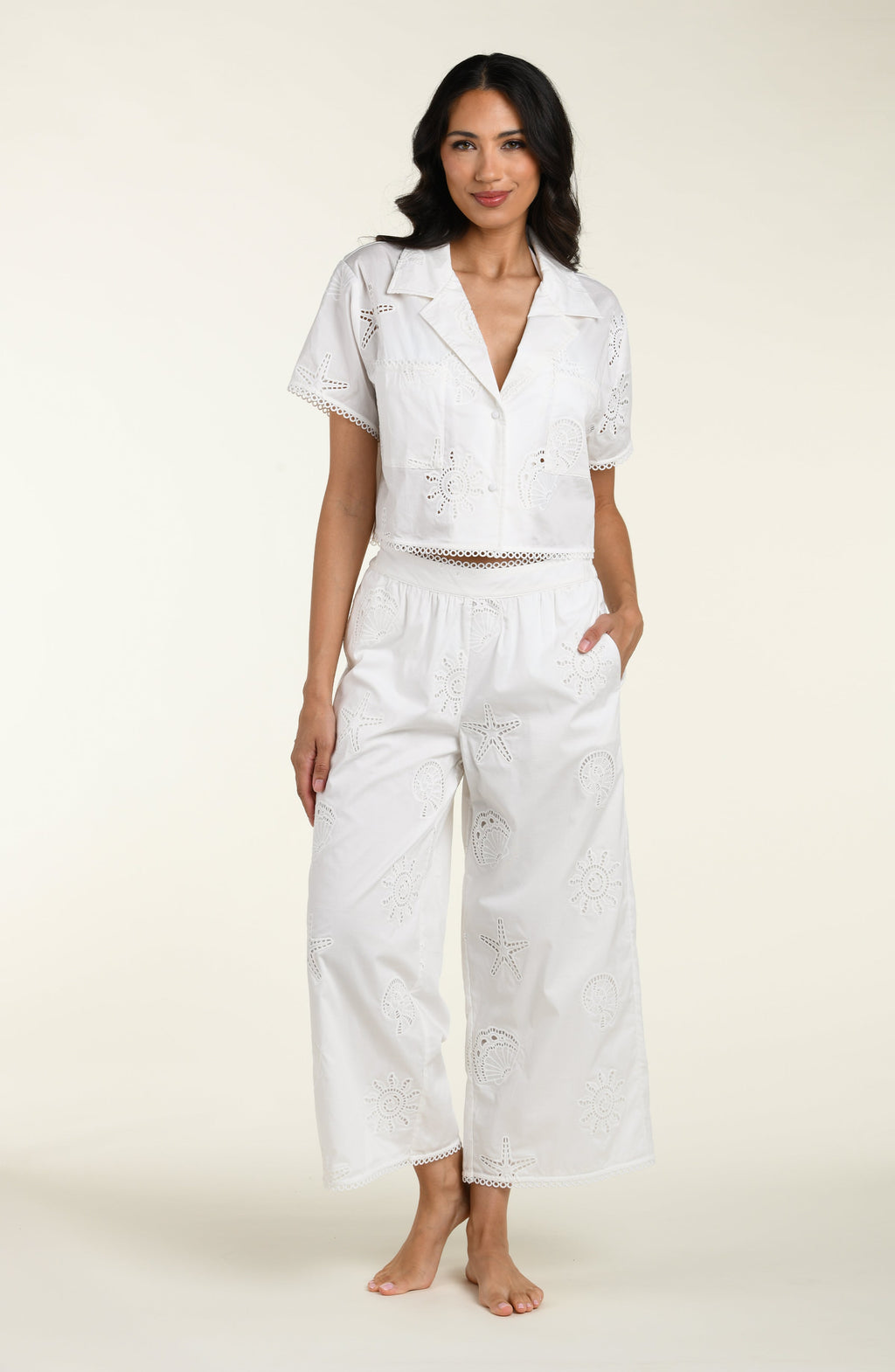Woman wearing a white cover up shirt with matching pants against a white background. 