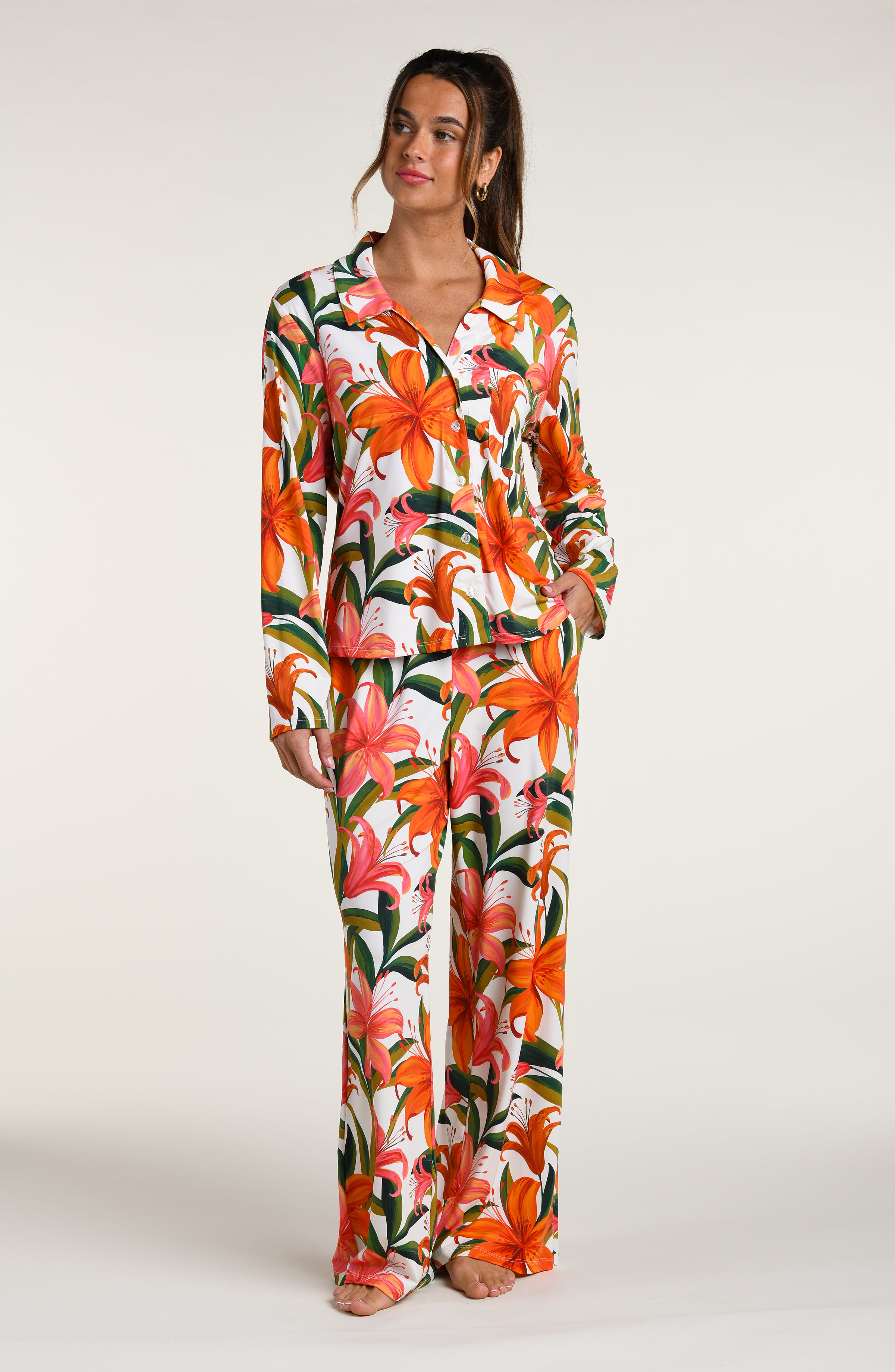Woman wearing a colorful tropical long sleeve and pant pajama set against a white background.