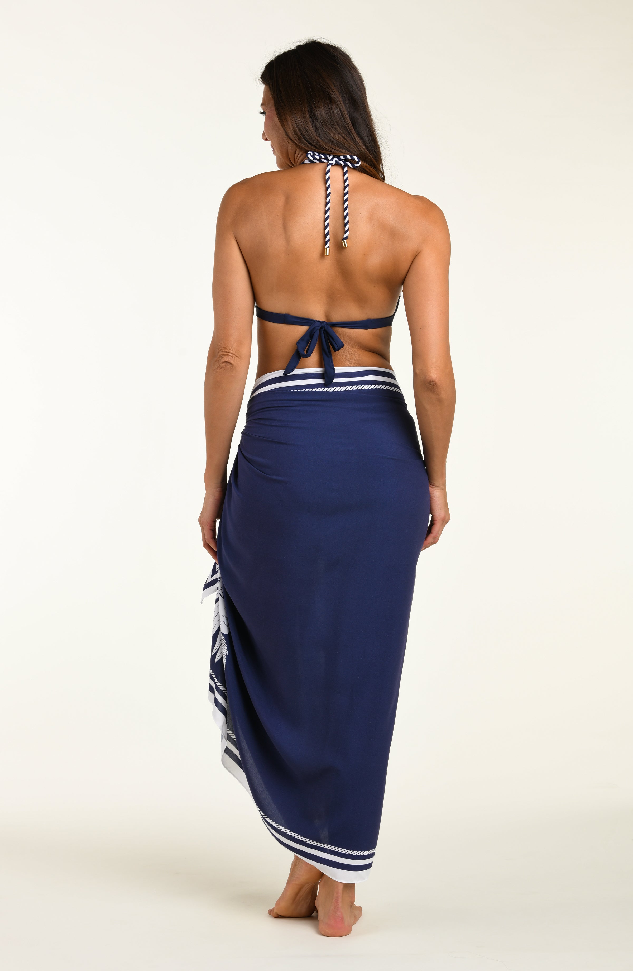 Person wearing a navy blue sarong with white floral patterns and a matching bikini top on a white background
