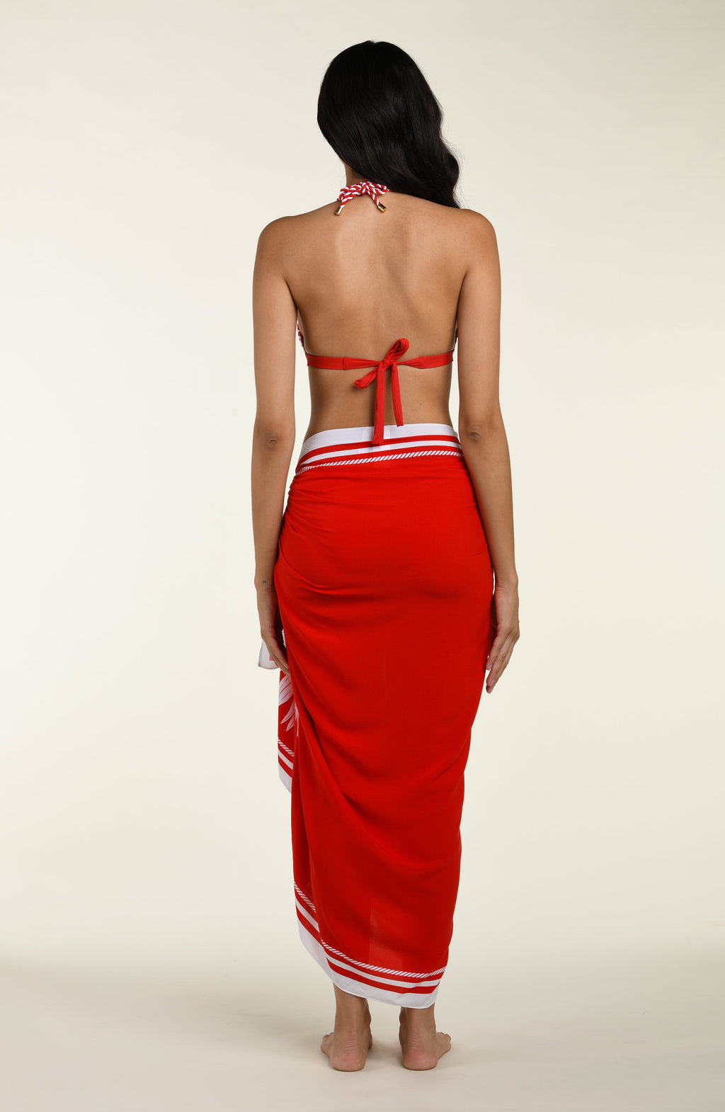 Woman wearing a red and white patterned sarong and a matching bikini top on a plain background