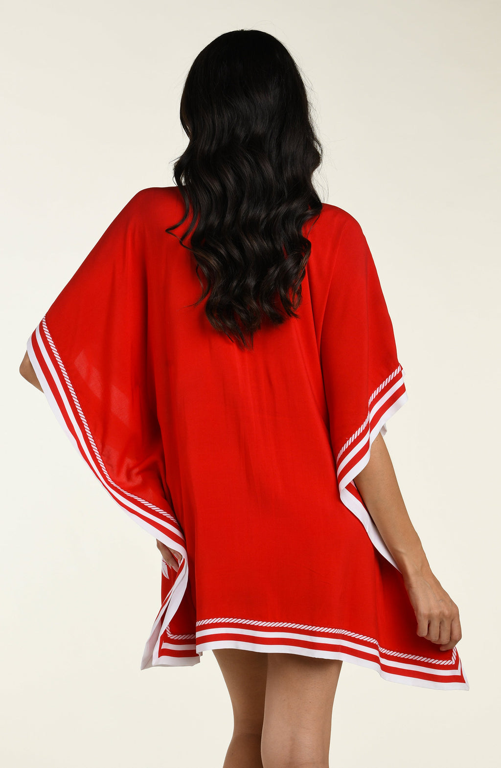Woman wearing a red floral tunic cover up with white accents on a beige background