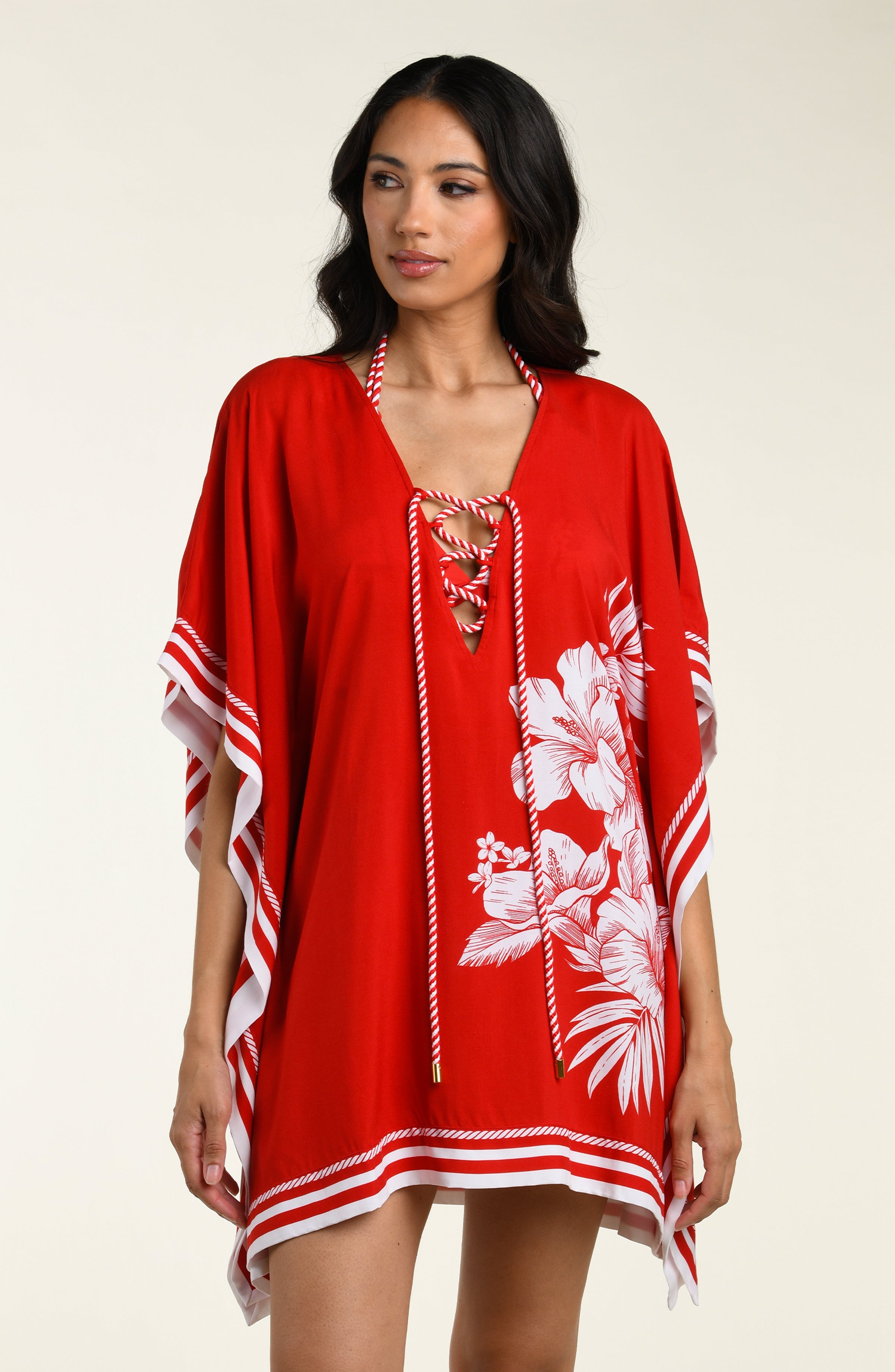 Woman wearing a red floral tunic cover up with white accents on a beige background