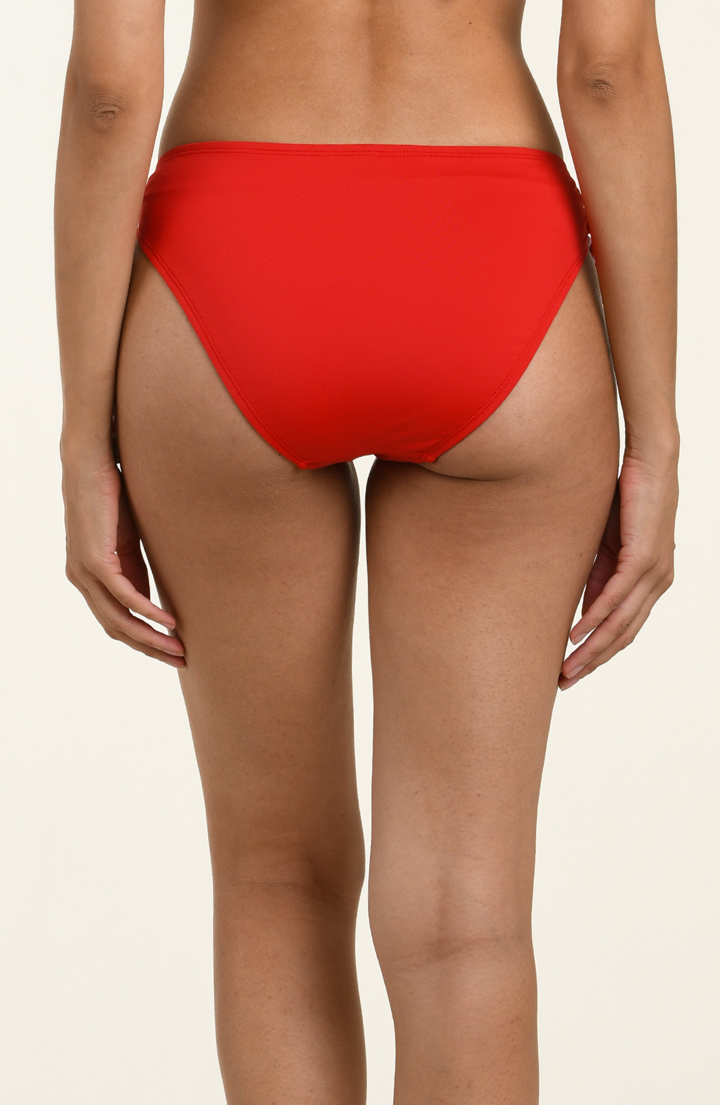 Red bikini bottom with white floral patterns and thin straps on a beige background