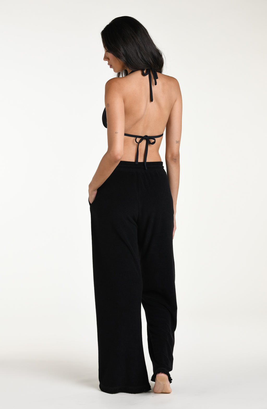 Woman wearing black cover up beach pants with a black bikini top against a white background. 