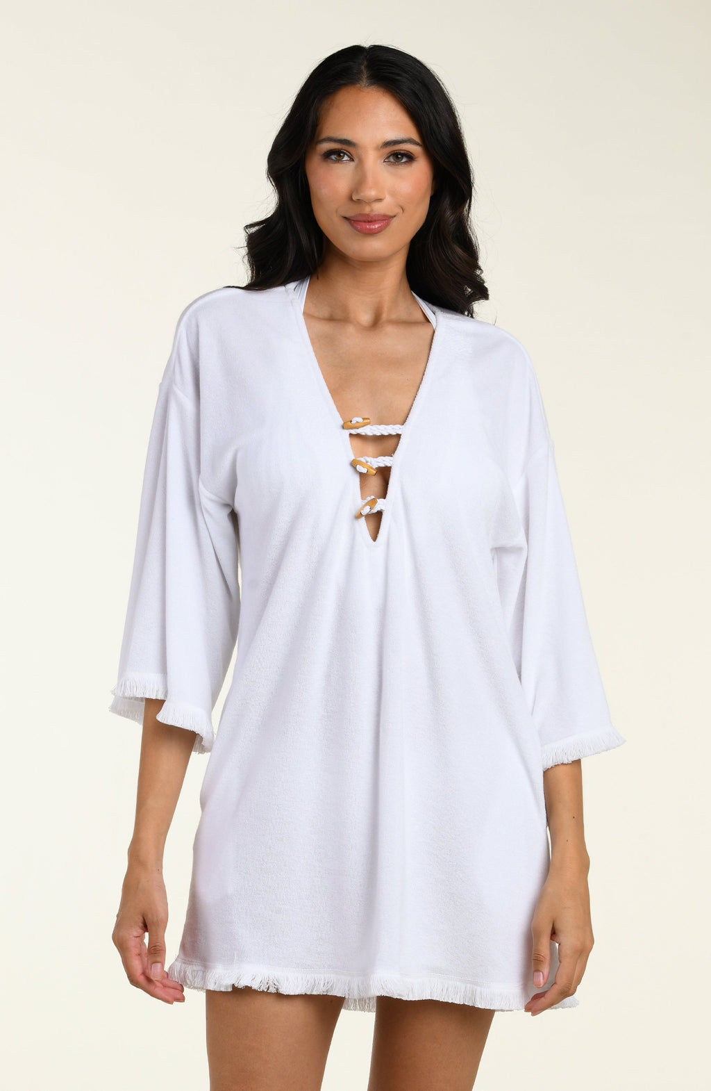 Woman wearing a white cover-up tunic  with lace-up front on a beige background