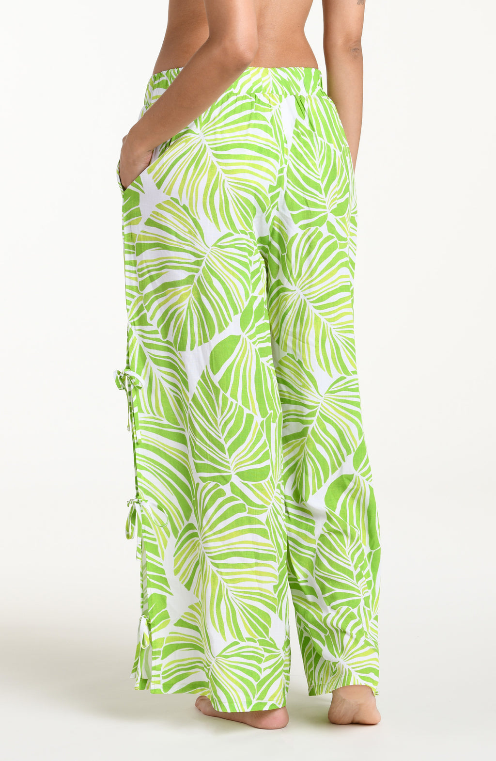 Woman wearing  green and white leaf-patterned beach pants against a white background