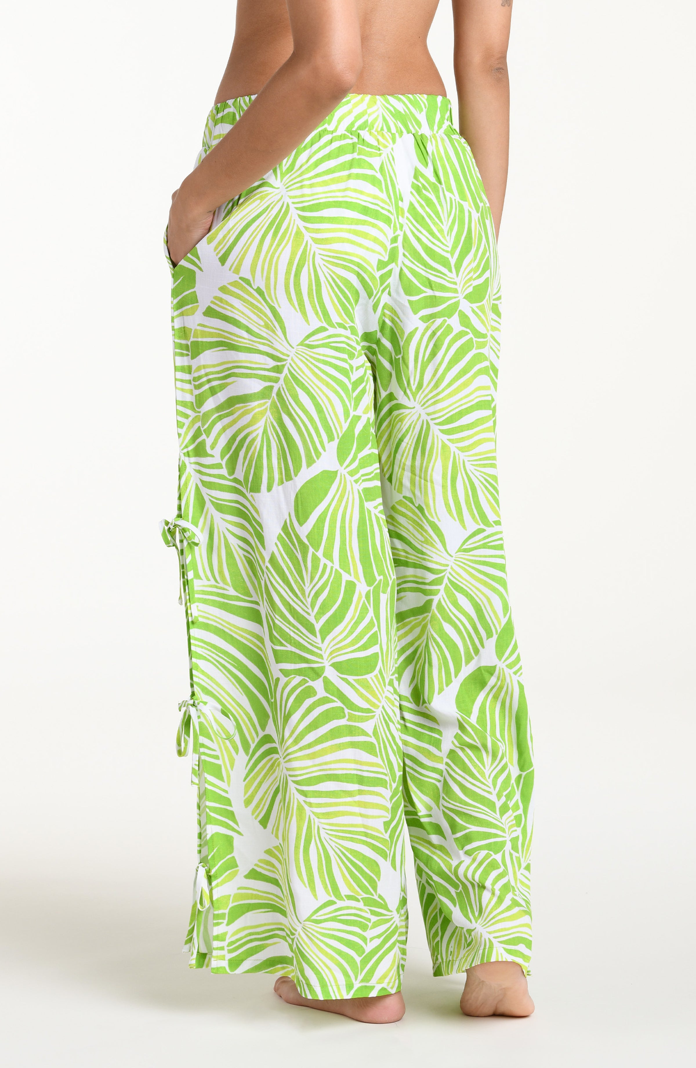 Woman wearing  green and white leaf-patterned beach pants against a white background