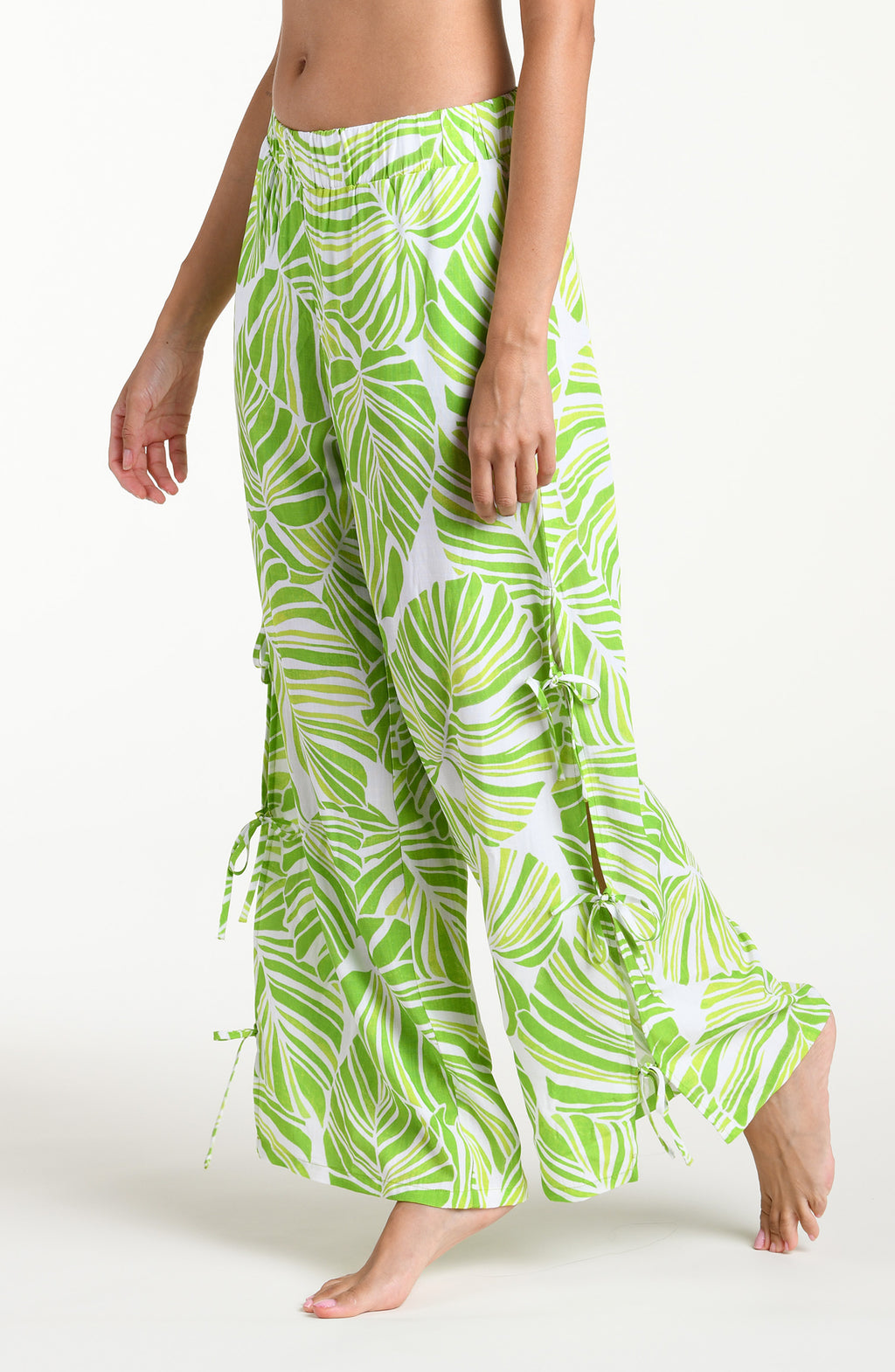 Woman wearing  green and white leaf-patterned beach pants against a white background