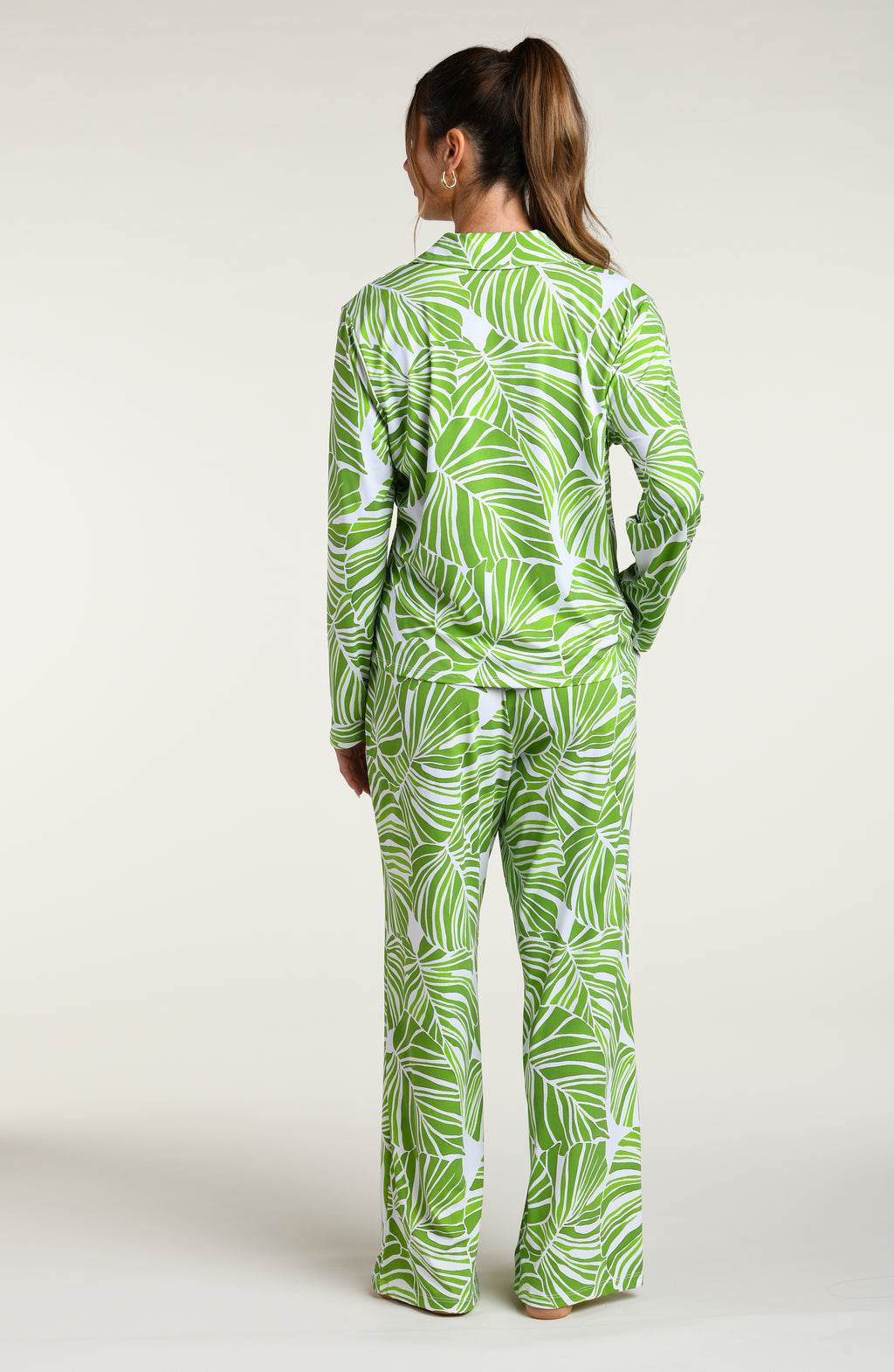 Woman wearing a green and white leaf-patterned pajama pant set against a plain white background.