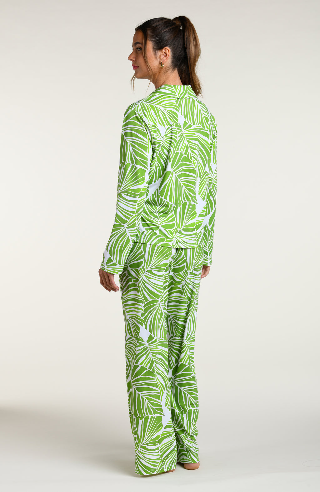 Woman wearing a green and white leaf-patterned pajama pant set against a plain white background.