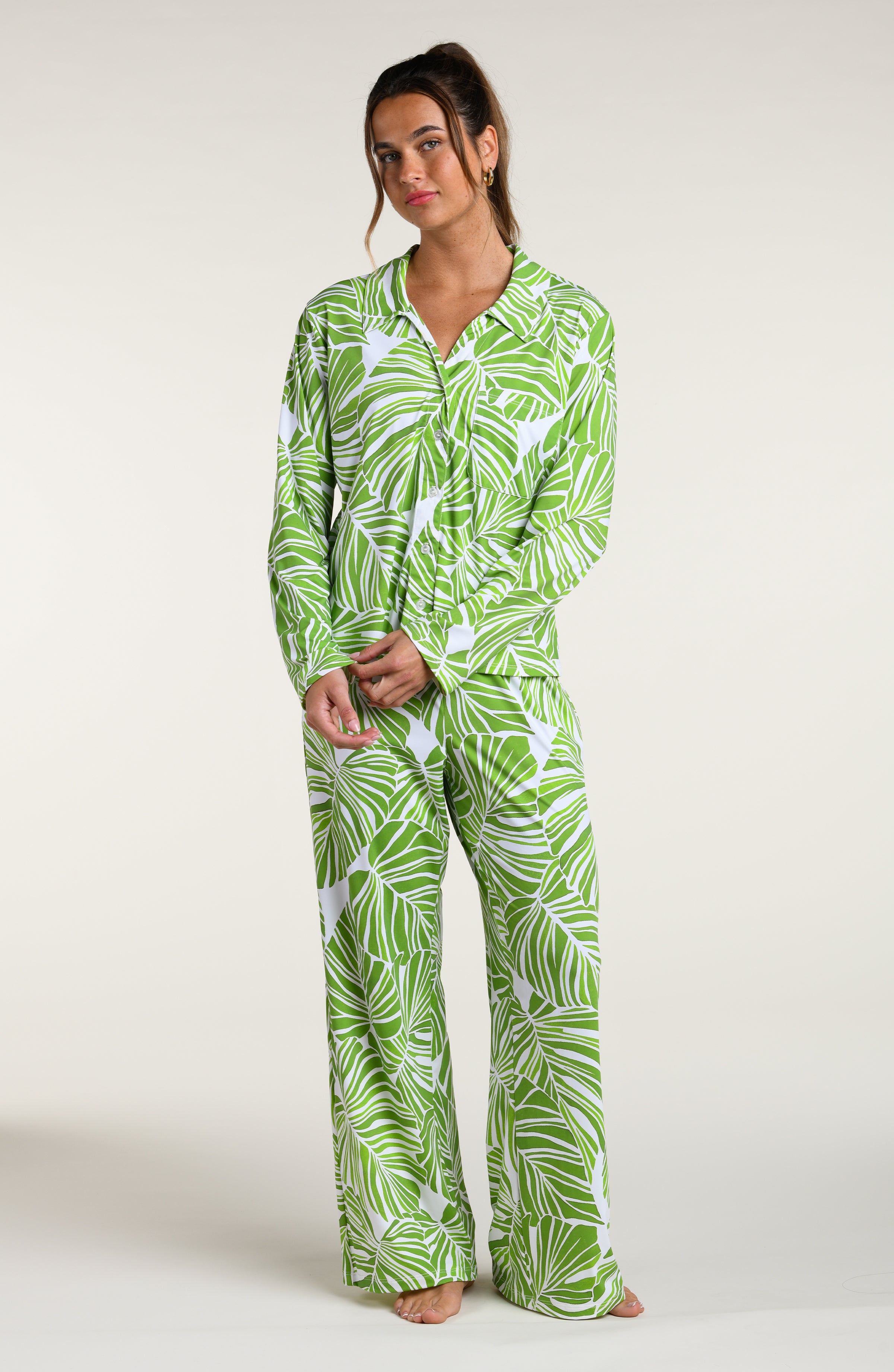 Woman wearing a green and white leaf-patterned pajama pant set against a plain white background.