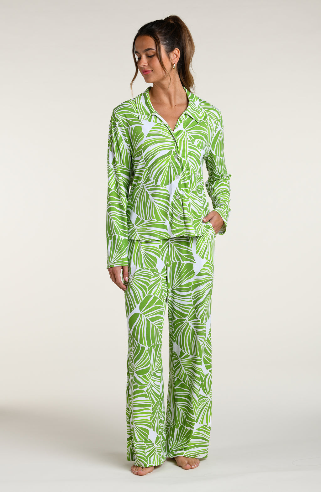 Woman wearing a green and white leaf-patterned pajama pant set against a plain white background.
