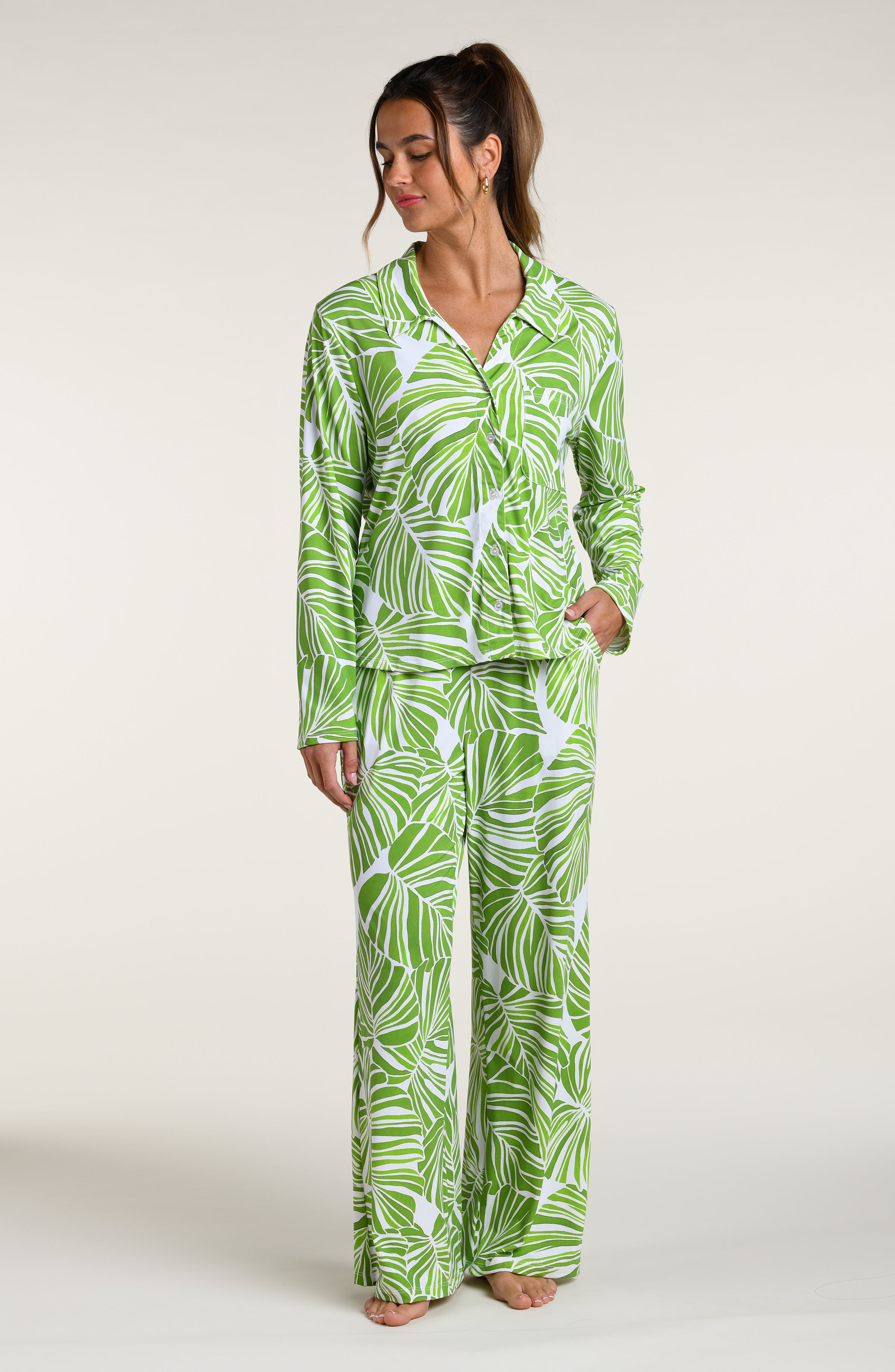 Woman wearing a green and white leaf-patterned pajama pant set against a plain white background.