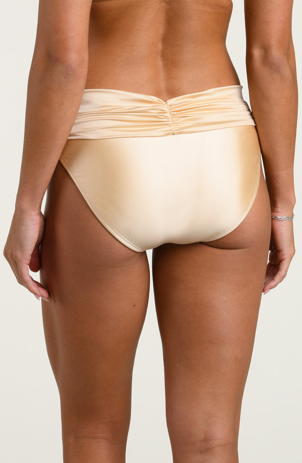 Woman wearing champagne colored bikini bottoms against a white background. 