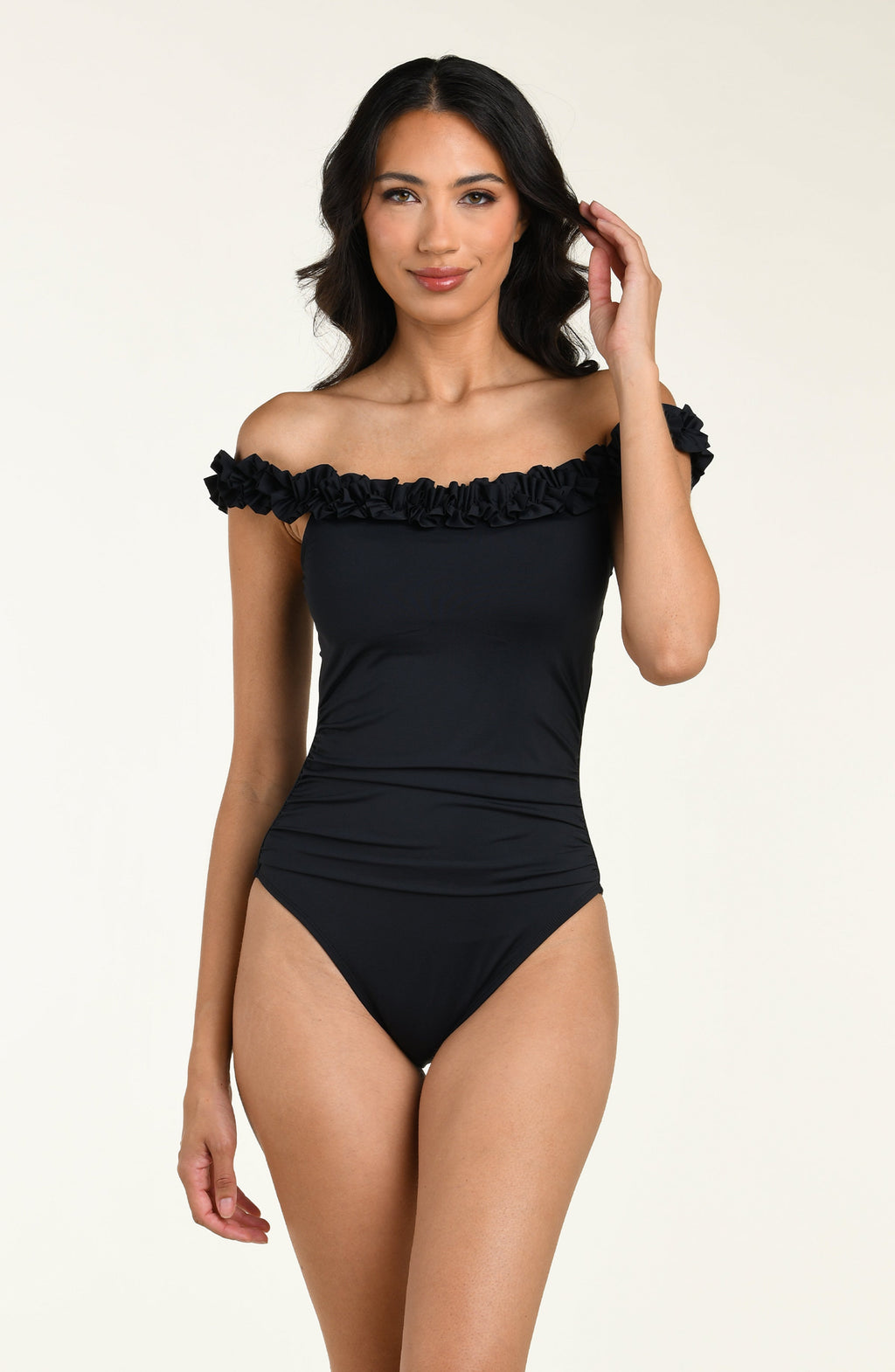 Woman wearing a black off-shoulder one piece swimsuit with ruffled details on a beige background