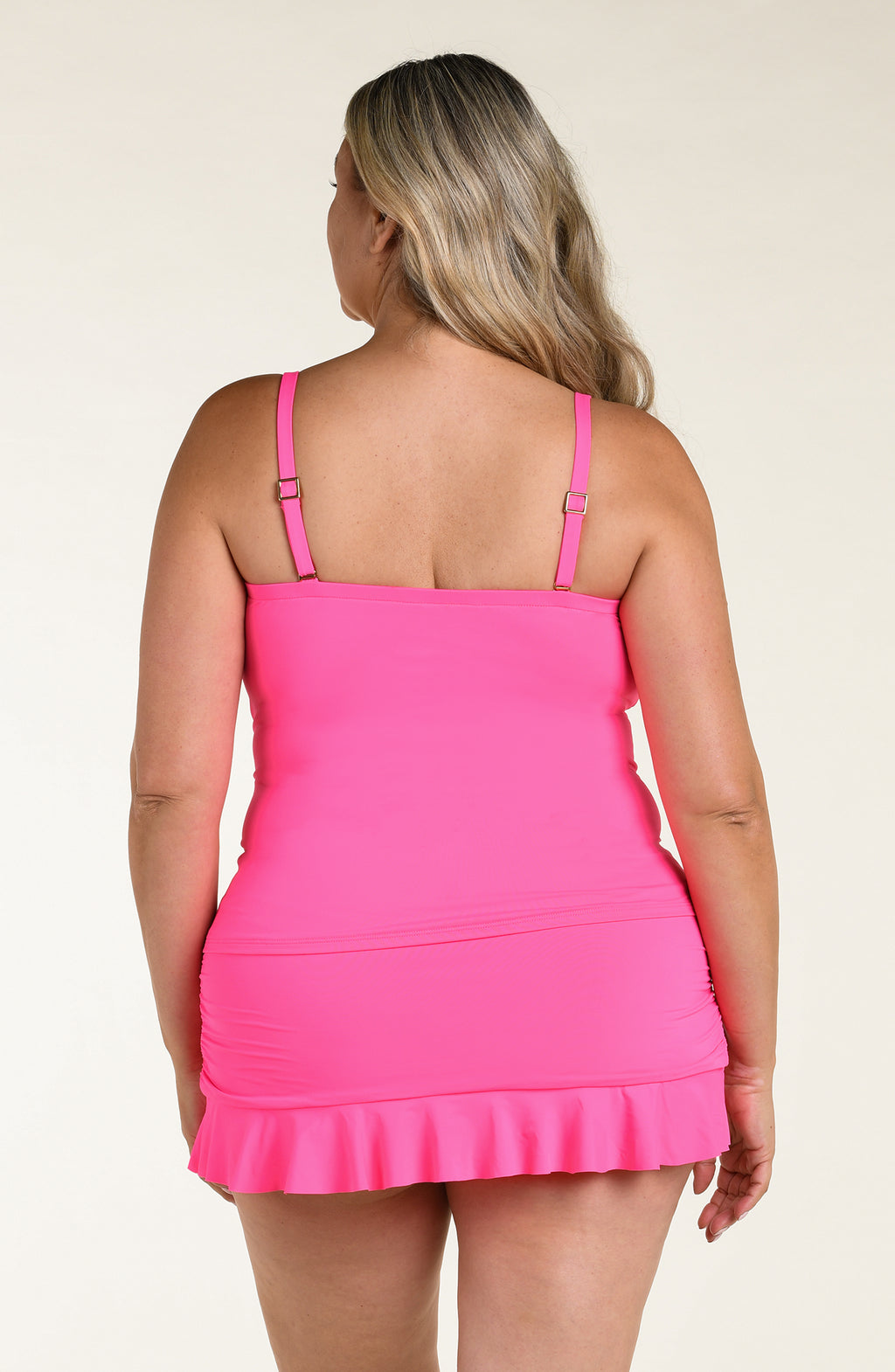 Woman wearing a pink ruffled tankini top and matching bottom against a beige background