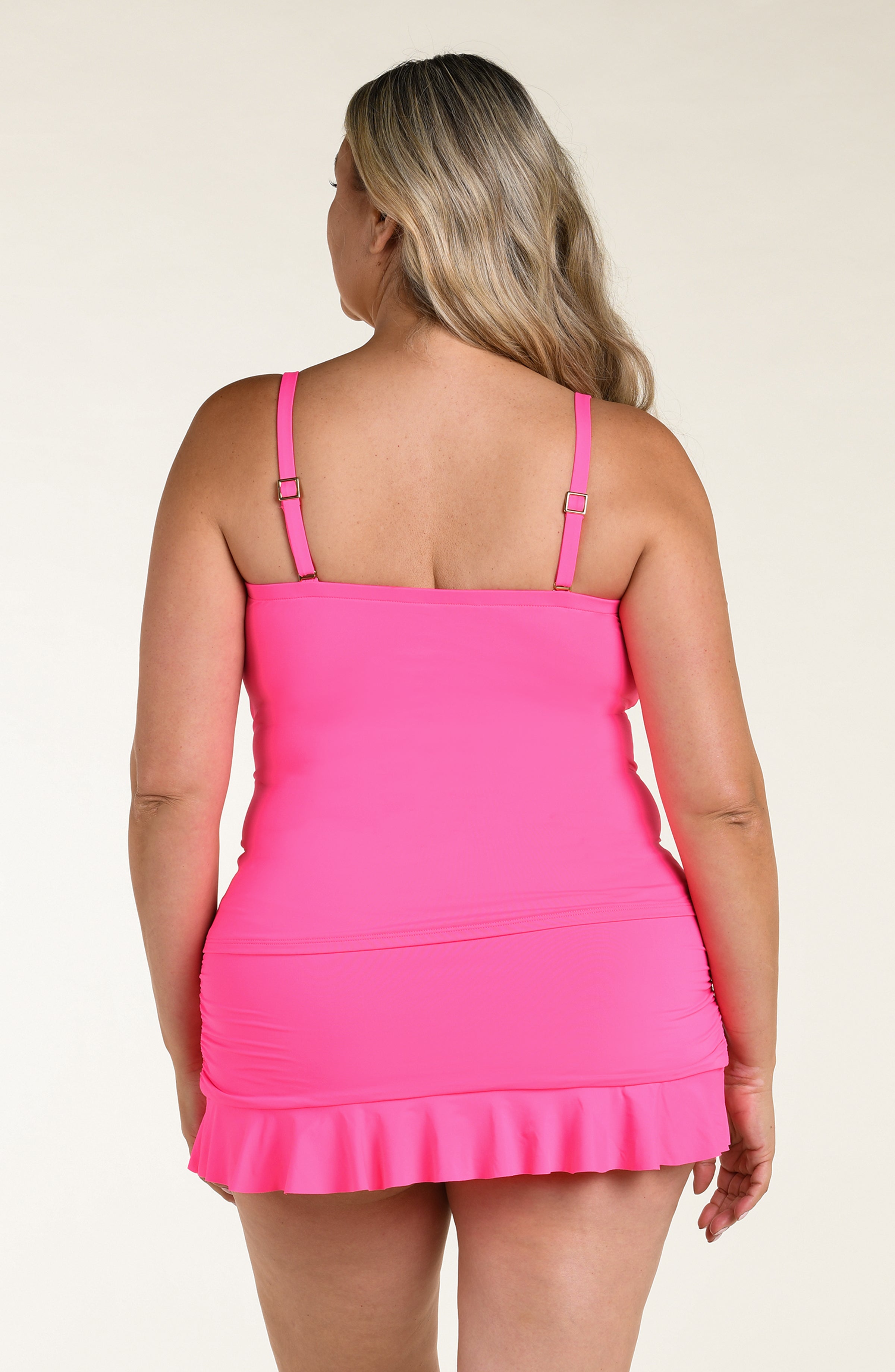 Woman wearing a pink ruffled tankini top and matching bottom against a beige background