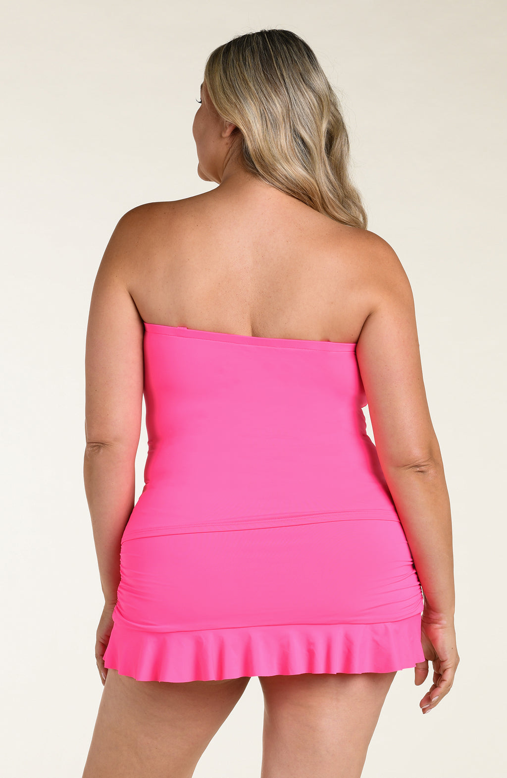 Woman wearing a pink ruffled tankini top and matching bottom against a beige background
