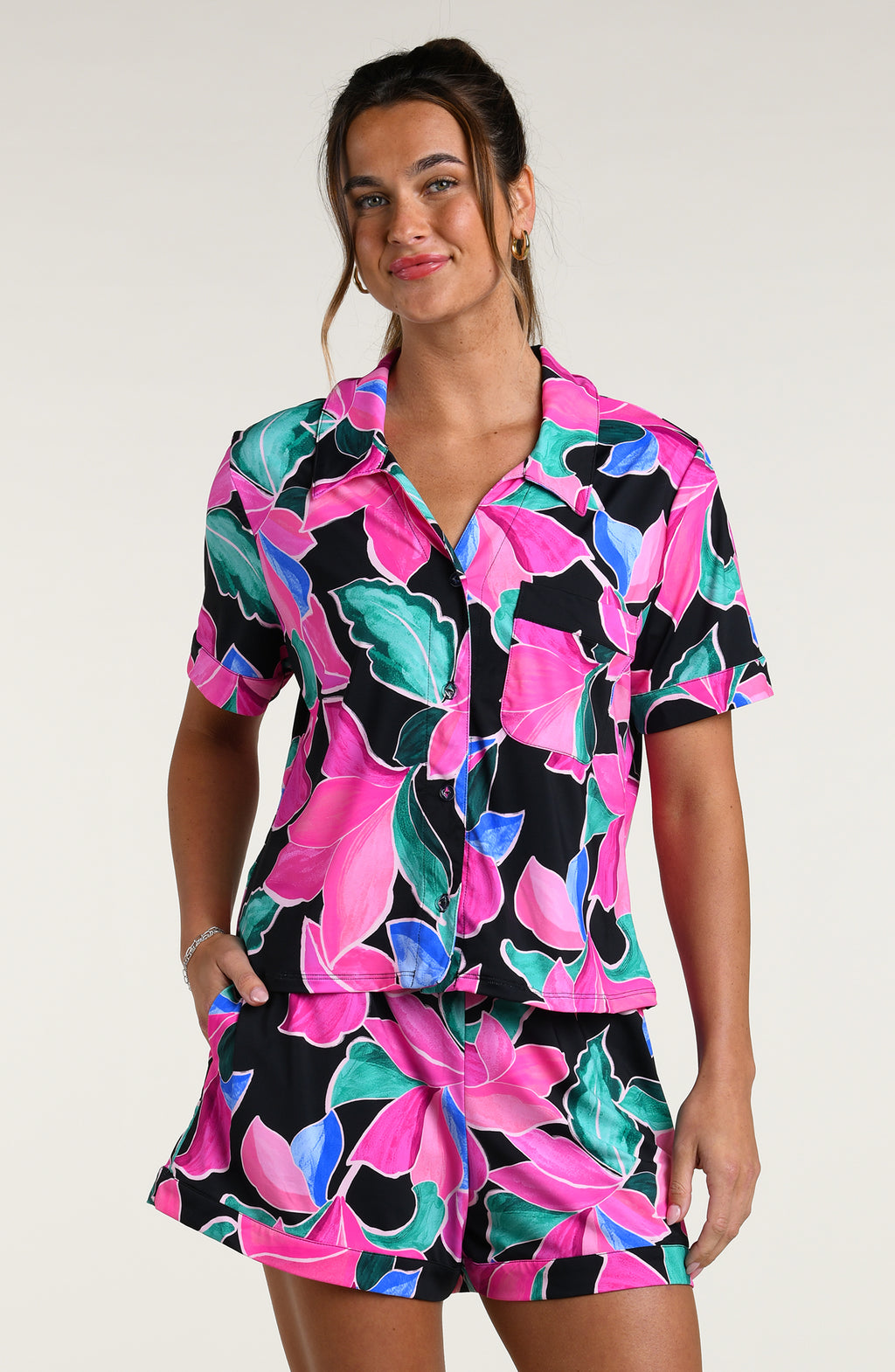 Woman wearing a colorful tropical patterned short sleeve top and shorts pajama set against a white background