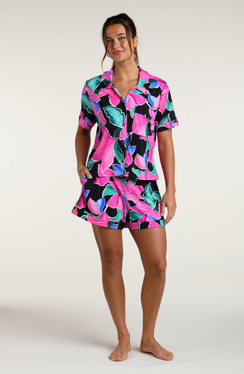 Woman wearing a colorful tropical patterned short sleeve top and shorts pajama set against a white background
