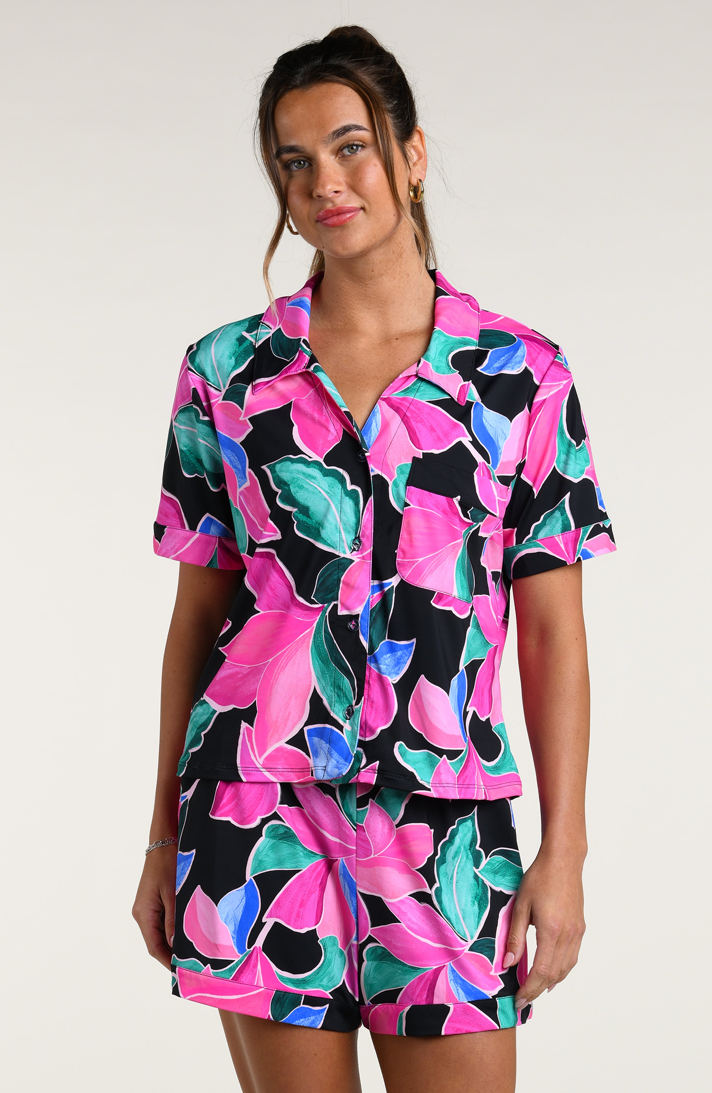 Woman wearing a colorful tropical patterned short sleeve top and shorts pajama set against a white background
