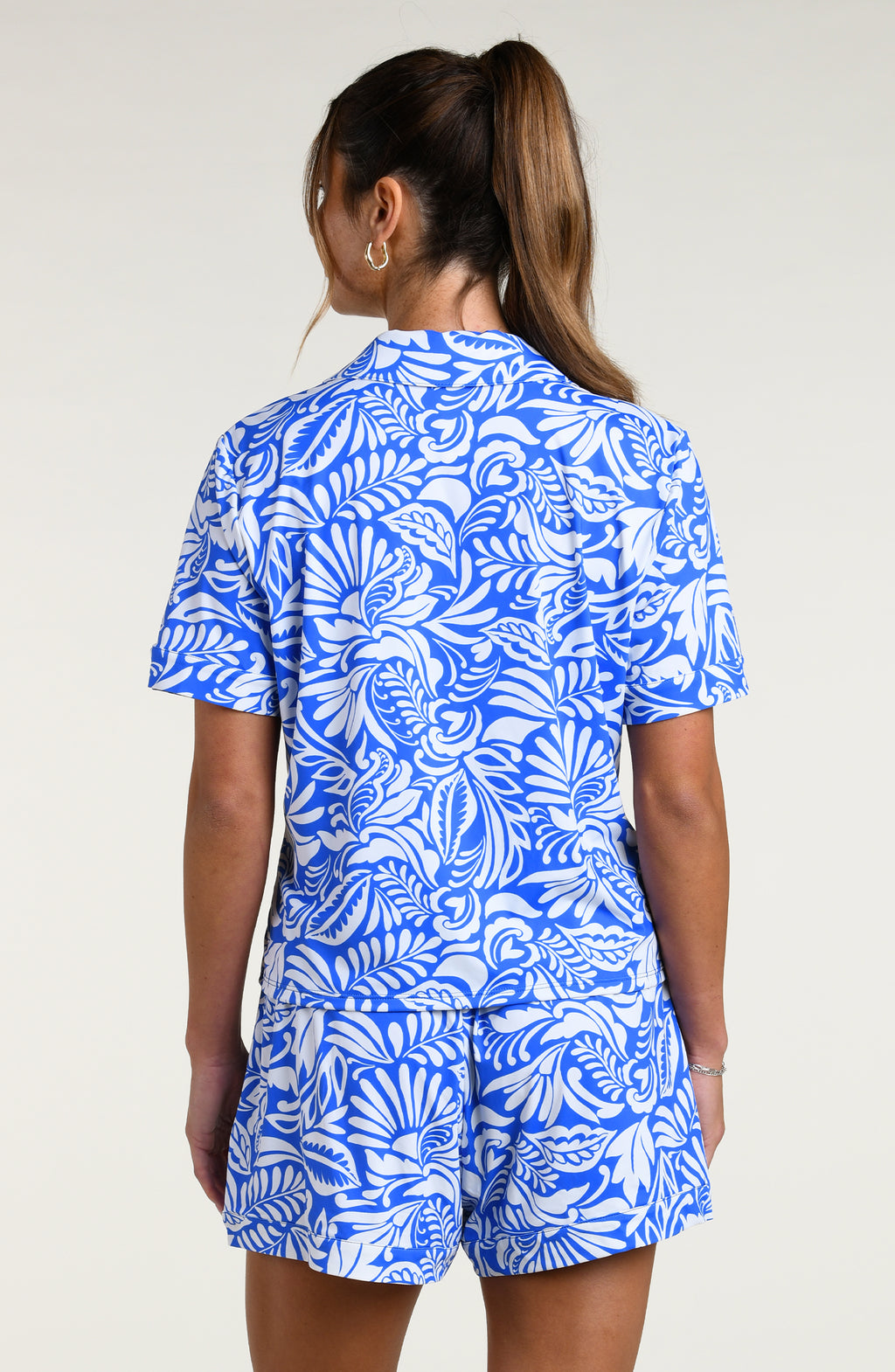 Woman wearing a blue and white patterned short sleeve shirt and shorts pajama set against a plain background