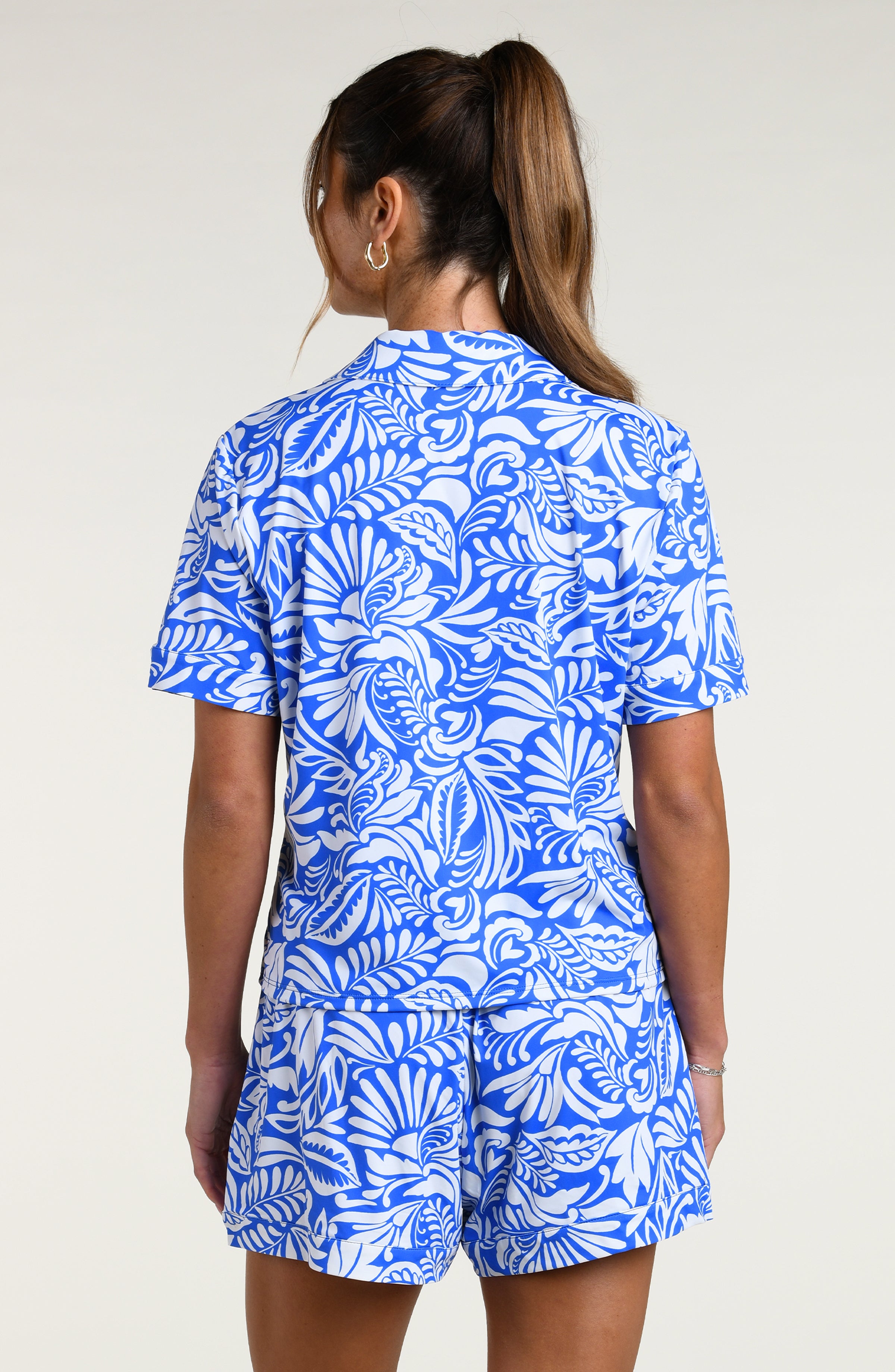 Woman wearing a blue and white patterned short sleeve shirt and shorts pajama set against a plain background