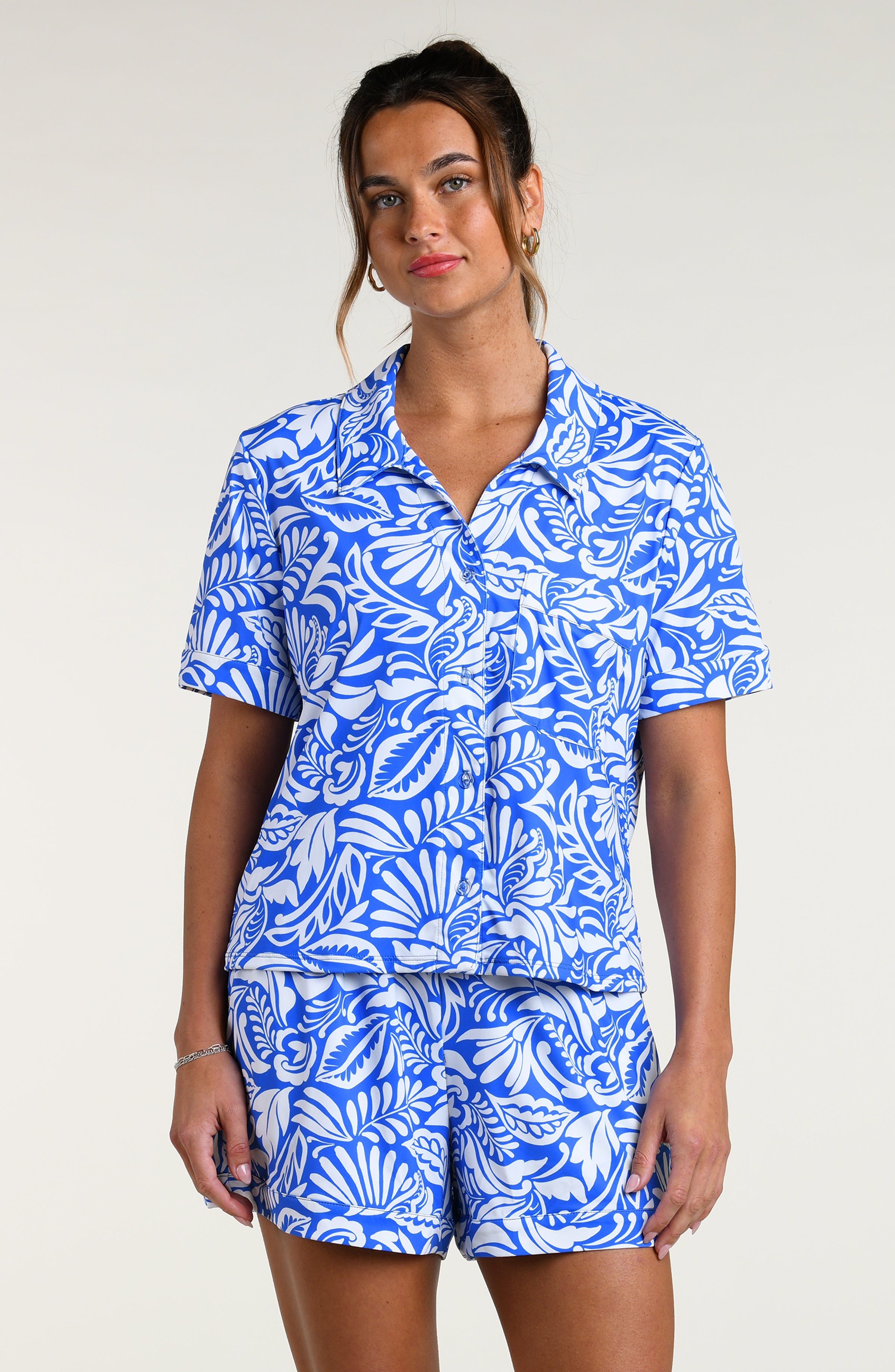 Woman wearing a blue and white patterned short sleeve shirt and shorts pajama set against a plain background