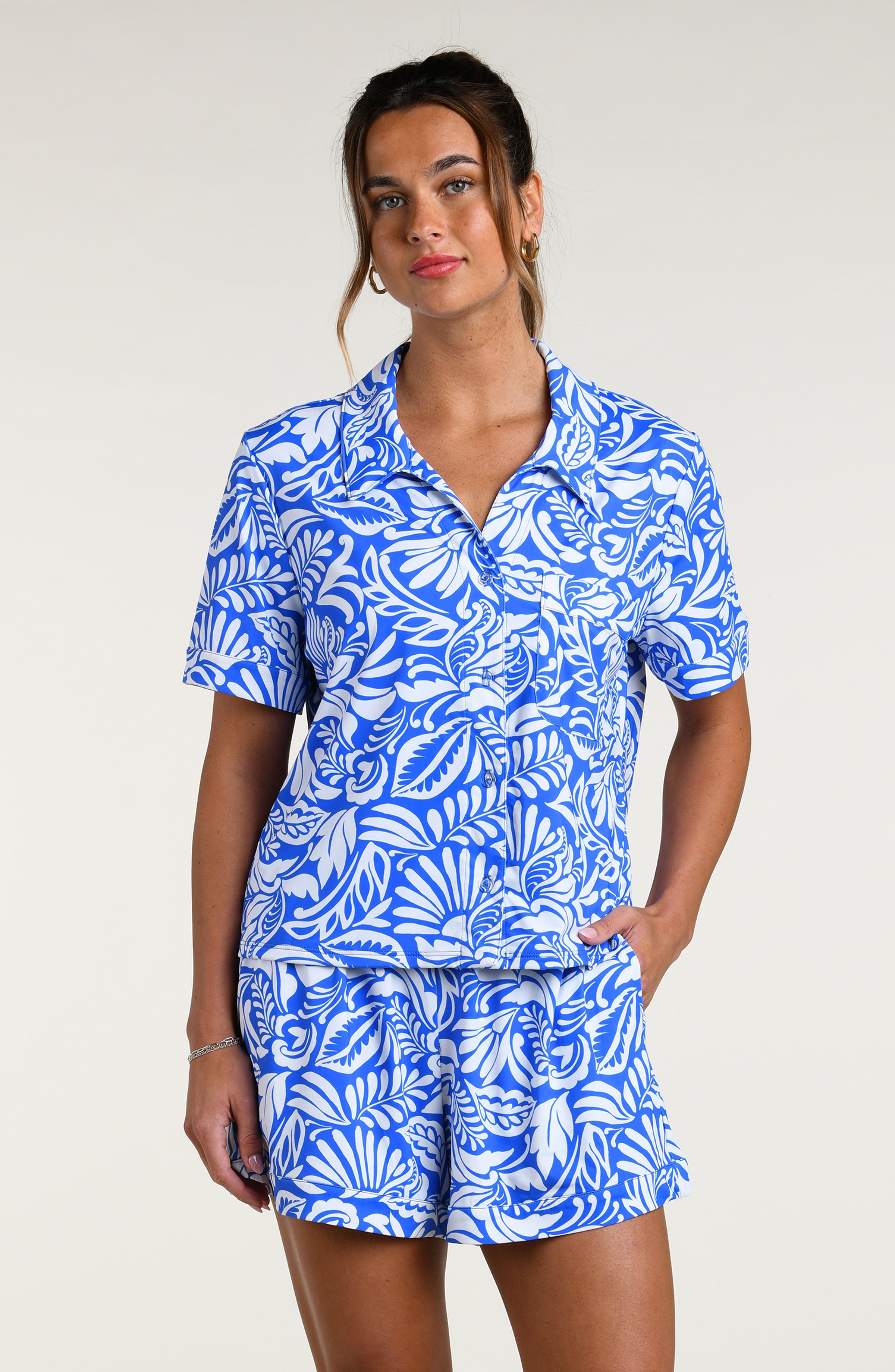 Woman wearing a blue and white patterned short sleeve shirt and shorts pajama set against a plain background