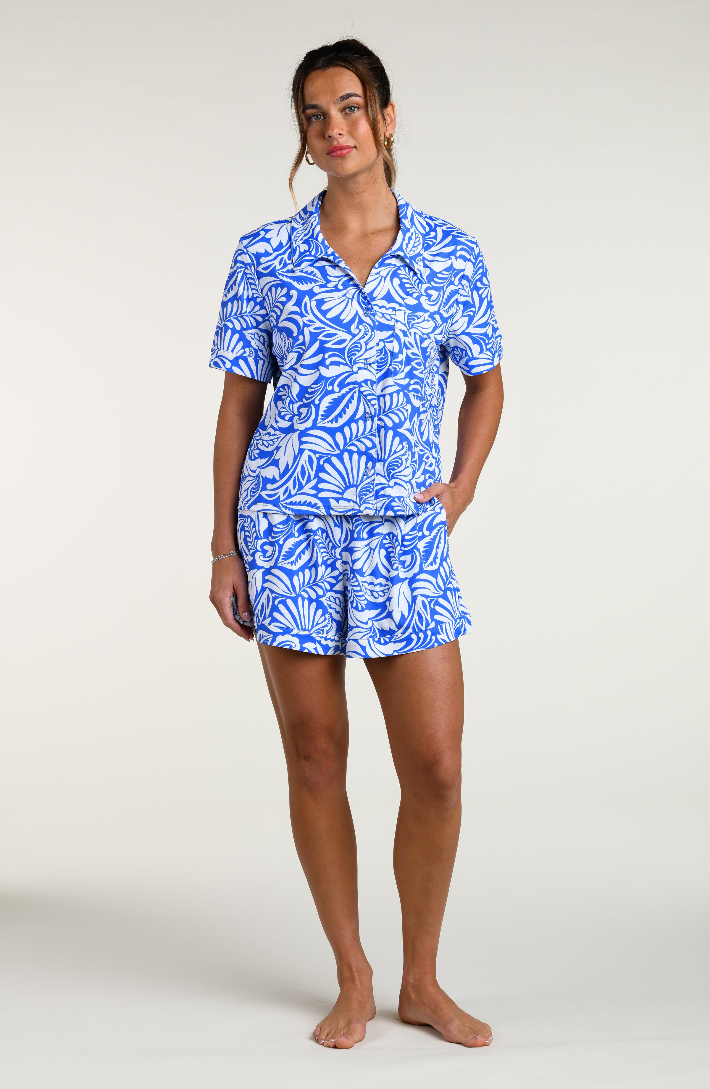 Woman wearing a blue and white patterned short sleeve shirt and shorts pajama set against a plain background