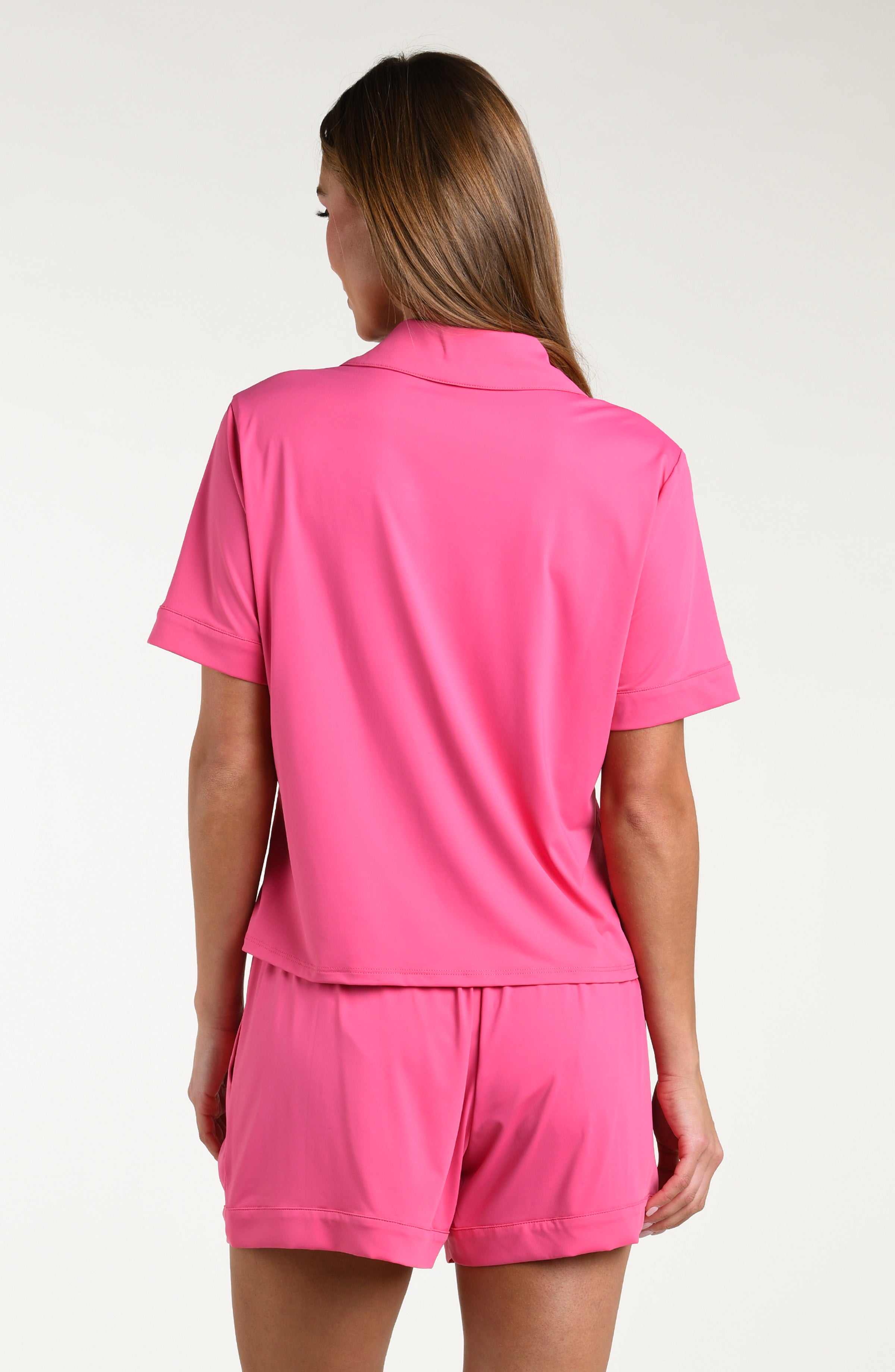 Woman wearing a bright pink pajama set with a matching shirt and shorts on a white background