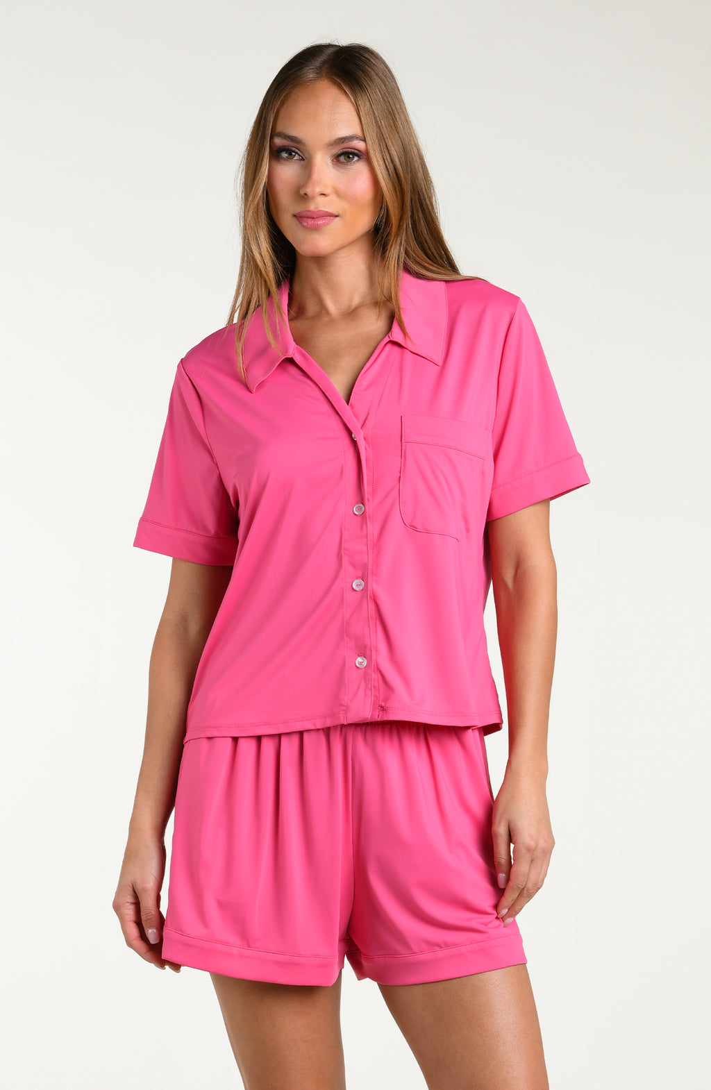 Woman wearing a bright pink pajama set with a matching shirt and shorts on a white background